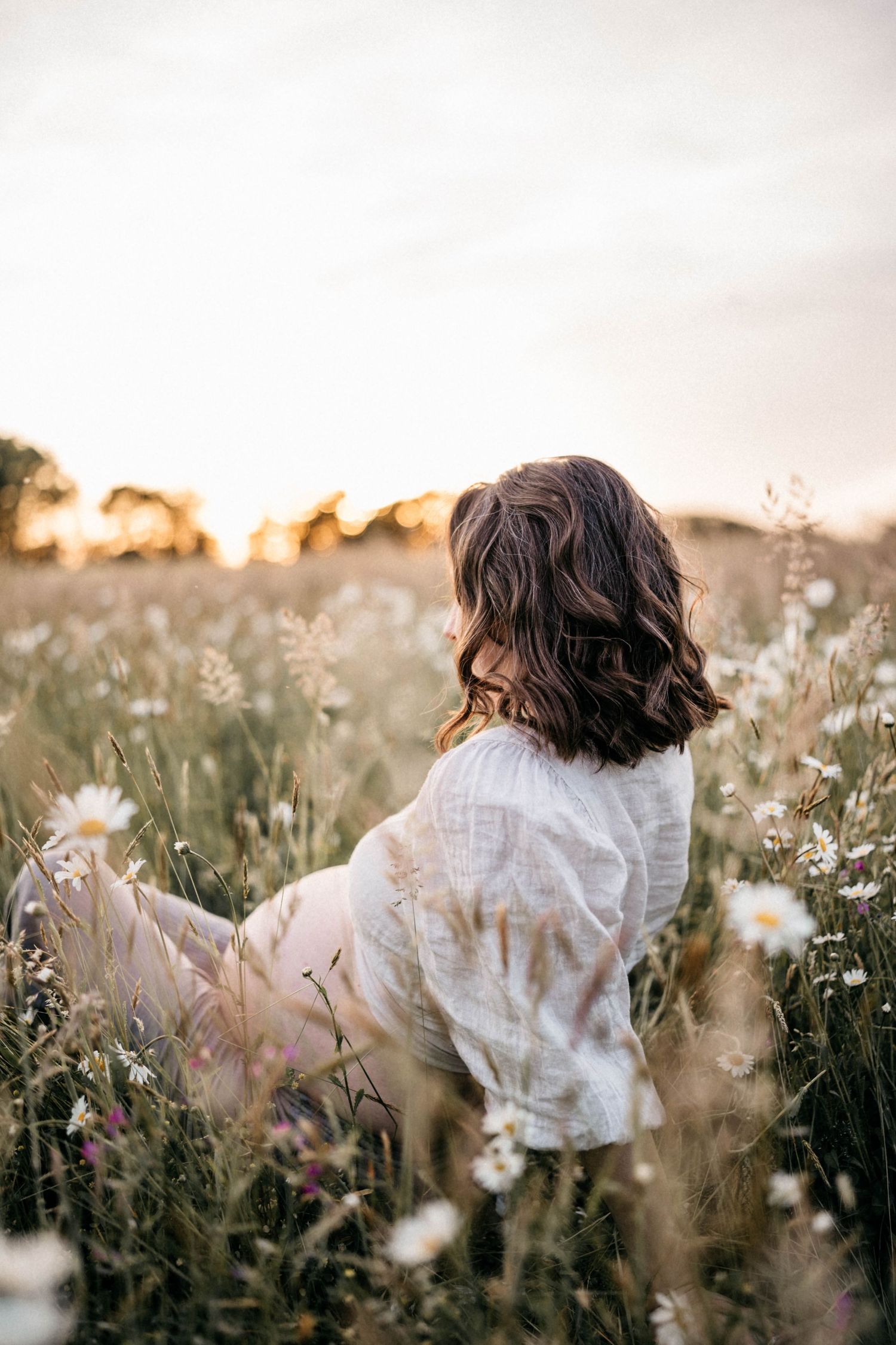 A white dress flows in the breeze among wildflowers at golden hour.
