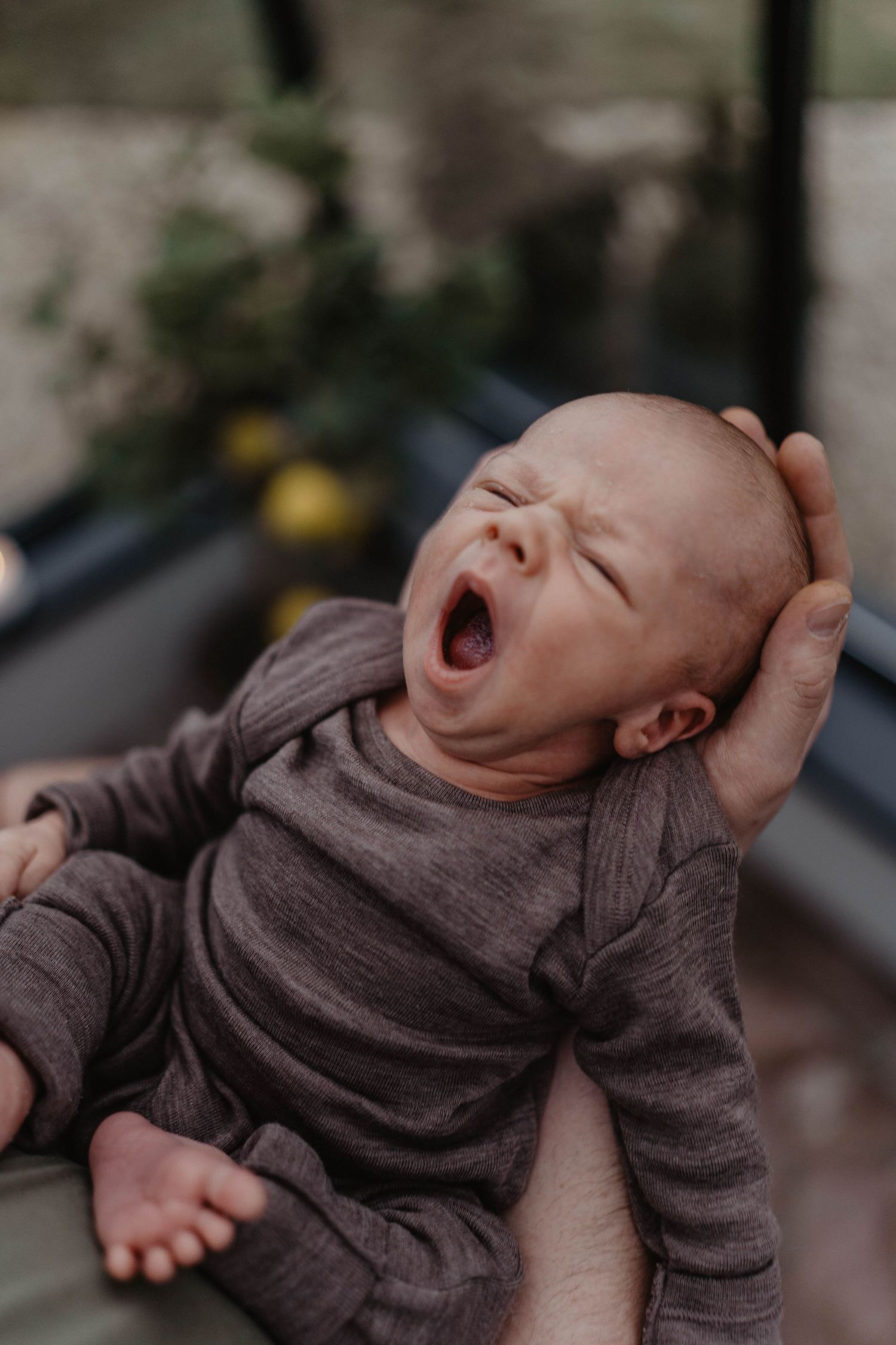 Baby in gray sweater yawning while being held.