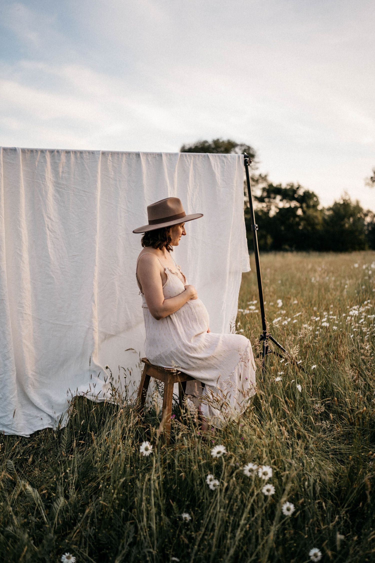 A white sheet backdrop hangs in a meadow with wildflowers as someone sits on a wooden stool.