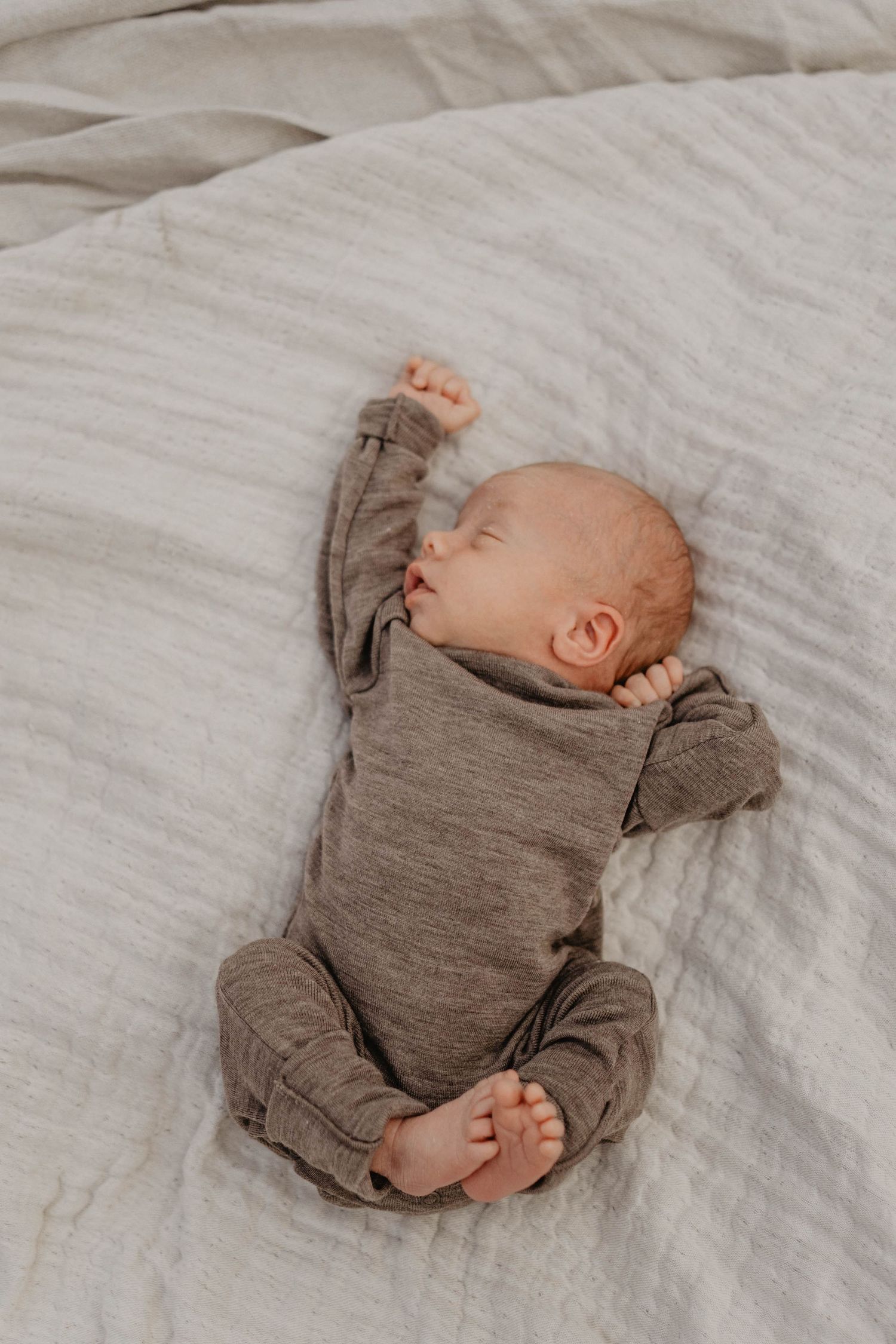 Newborn baby in gray onesie sleeping peacefully on white bedding.