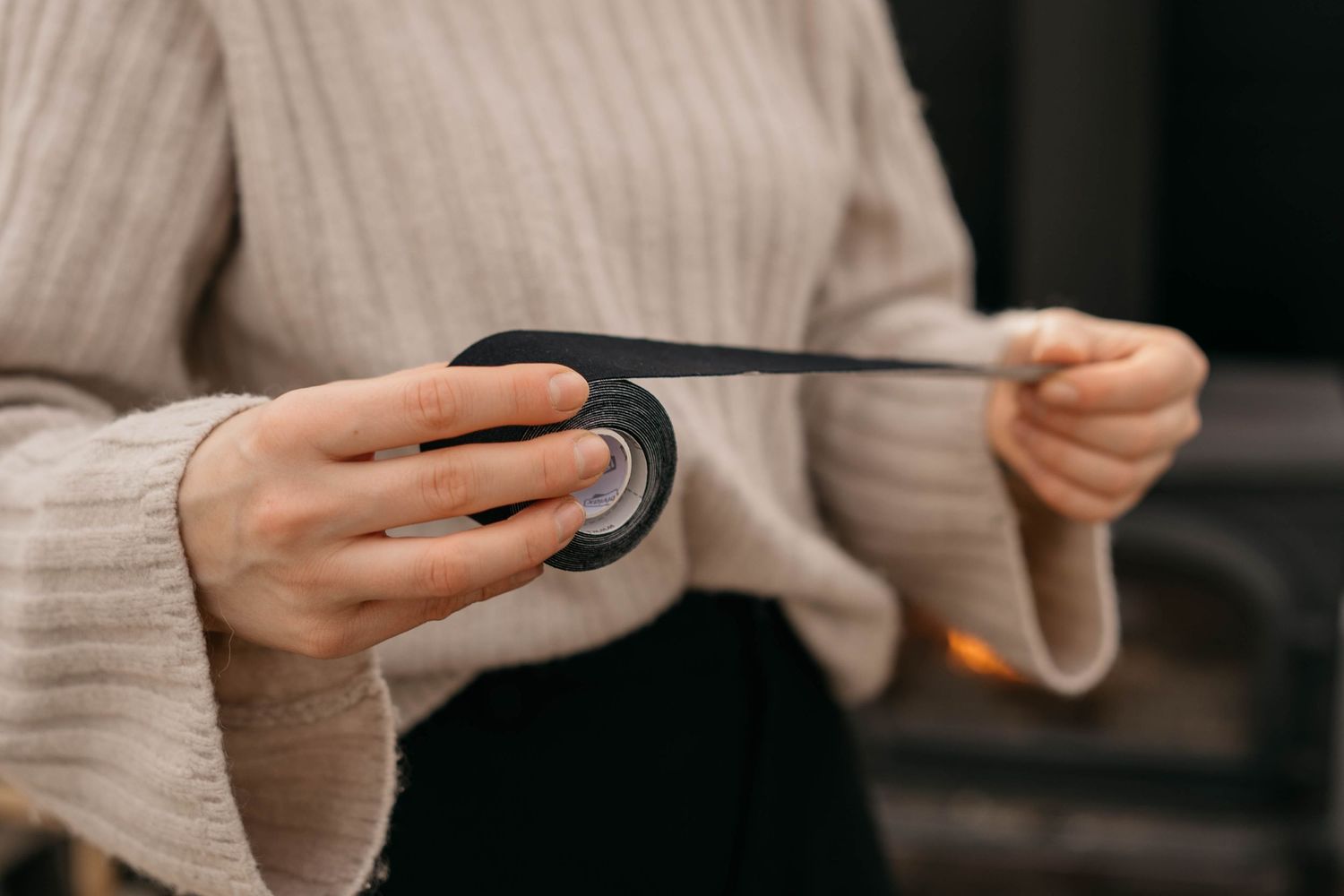 Person in beige sweater holding and wrapping a black USB cable or charging cord.