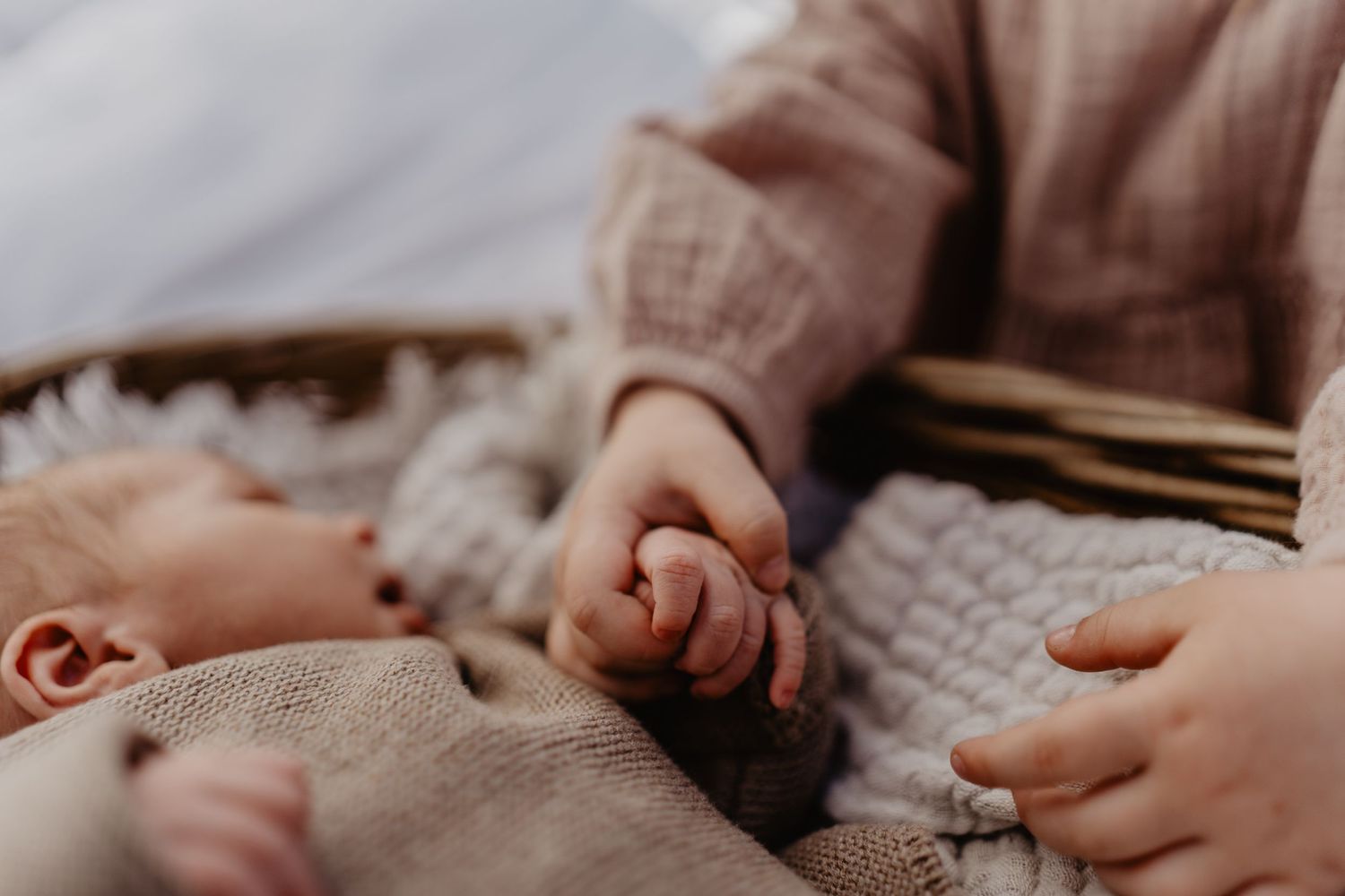 Close up of tiny baby hand reaching out while laying on soft knit blanket in warm lighting.