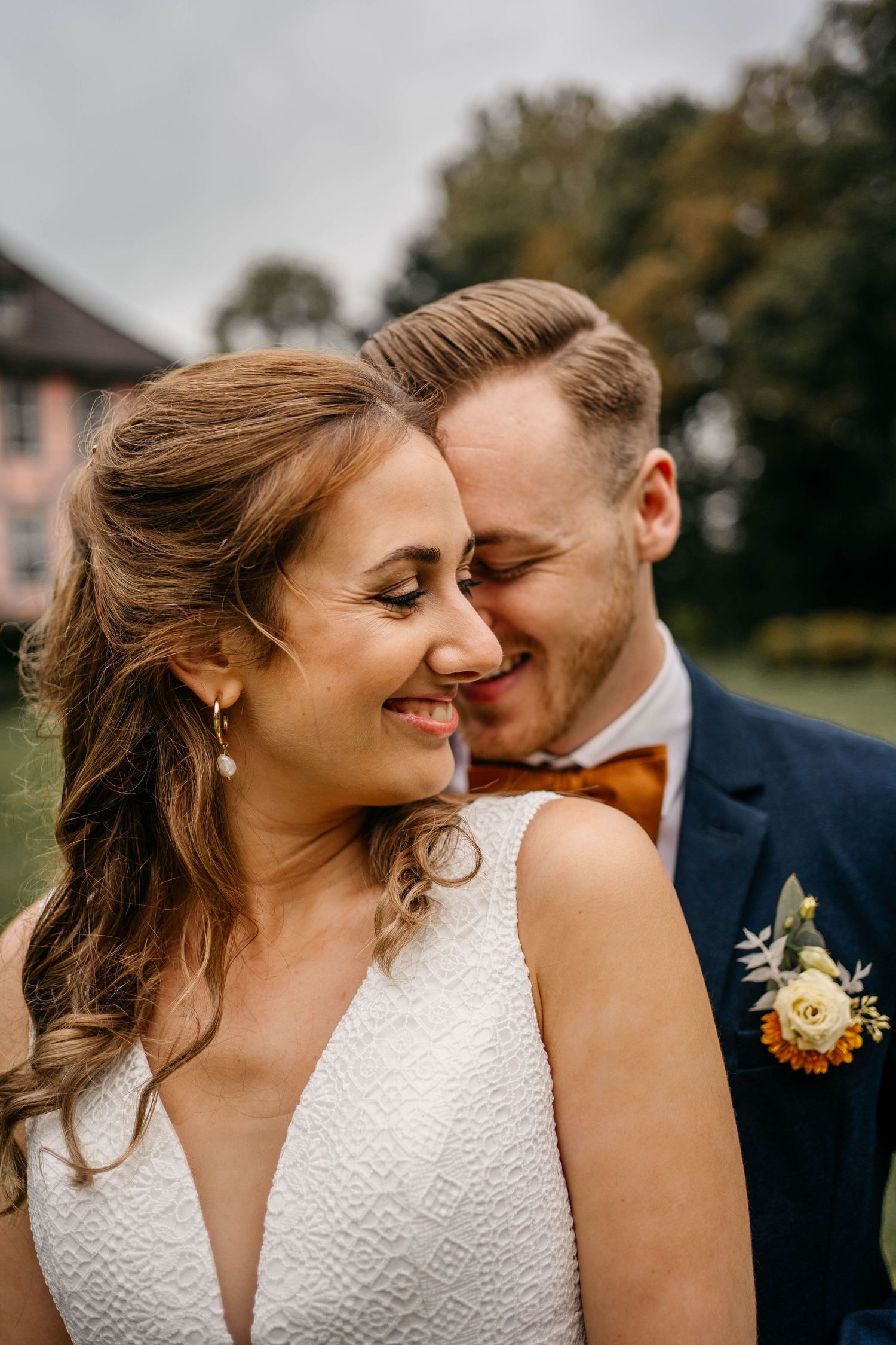Close intimate portrait of newlyweds smiling together outdoors, bride in white dress with groom in navy suit.