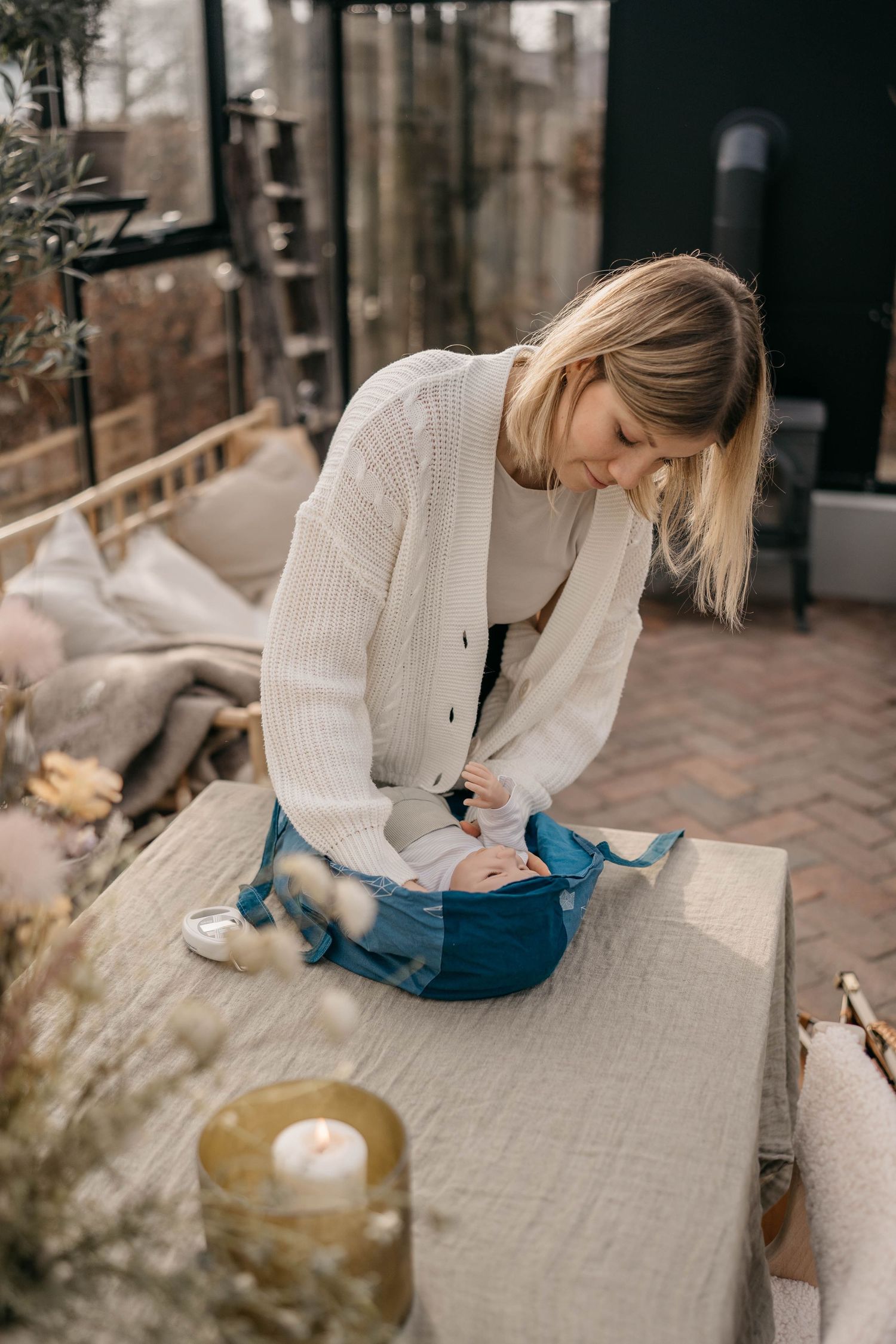 Writing in a cozy outdoor setting with white sweater and jeans while sitting on a stone bench with candle nearby.