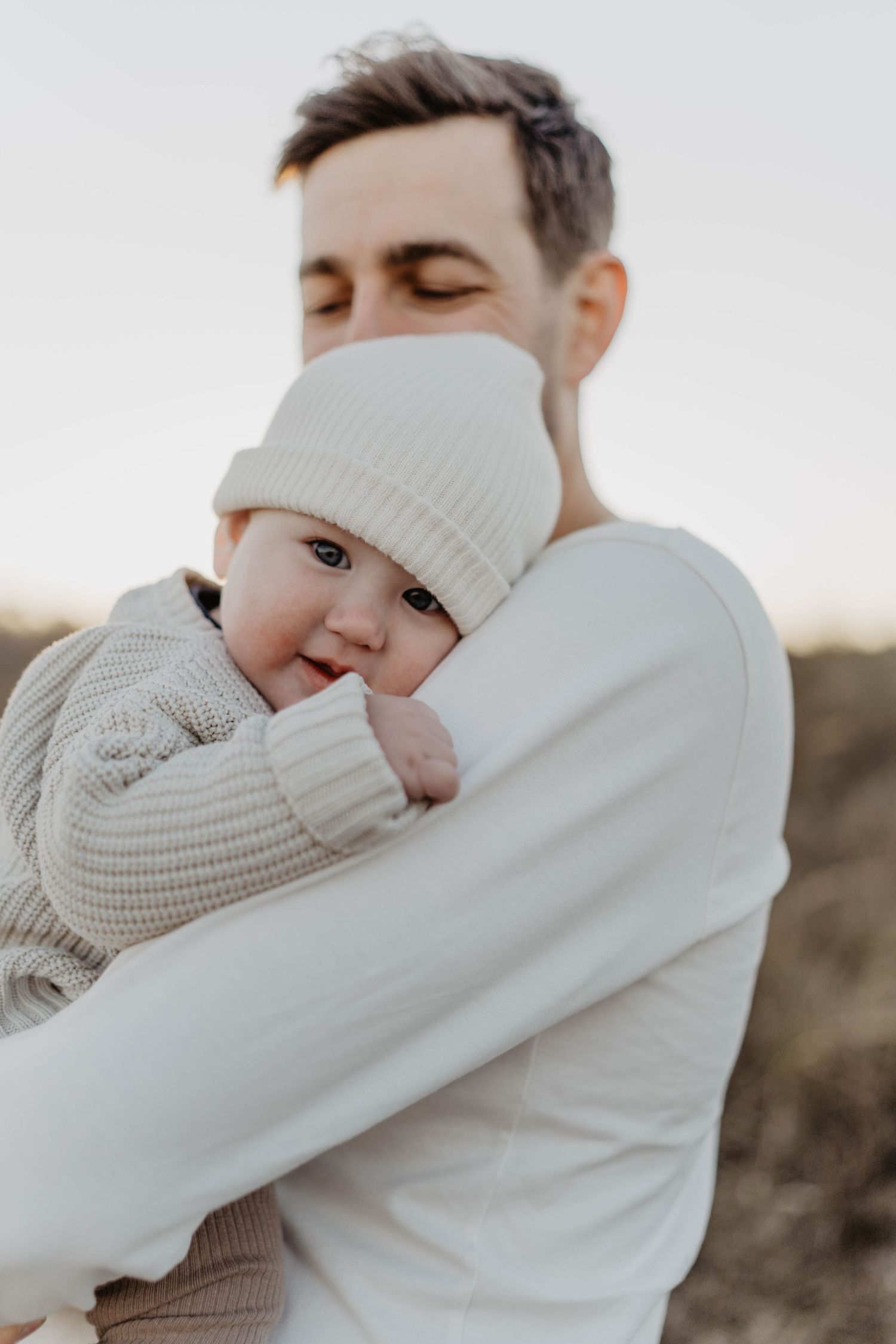 Close-up portrait of baby in knit beanie being held in white sweater.