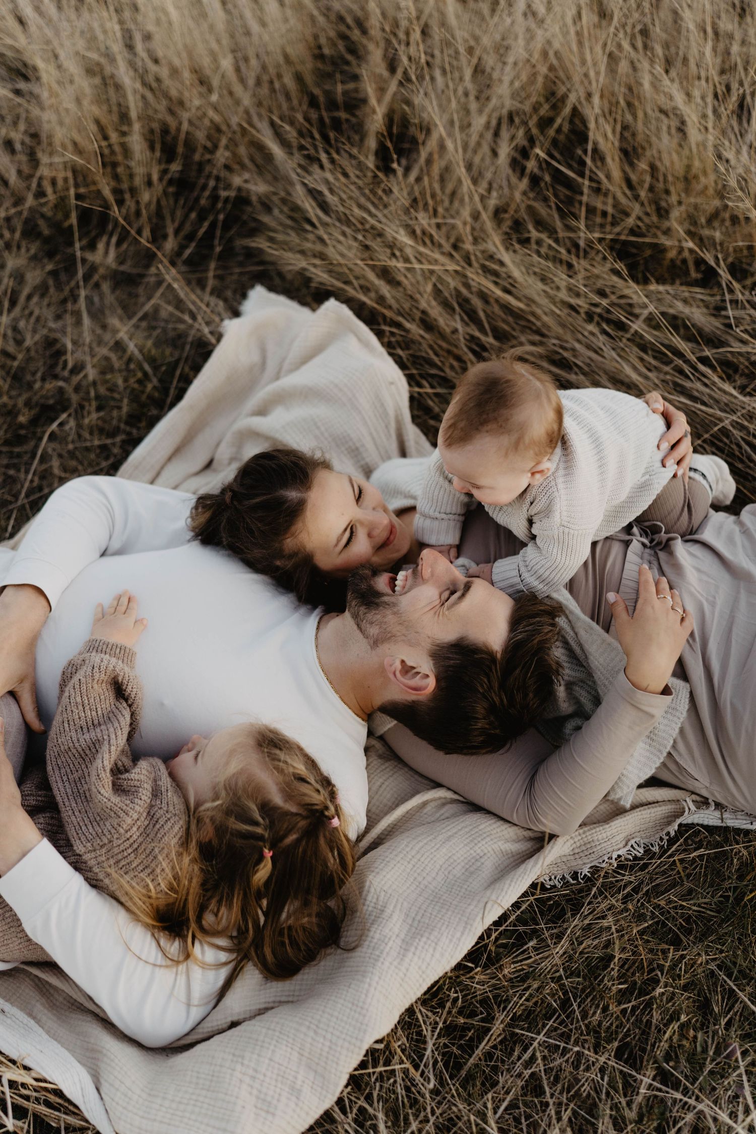 Family lying on blanket in tall grass sharing intimate moment together.