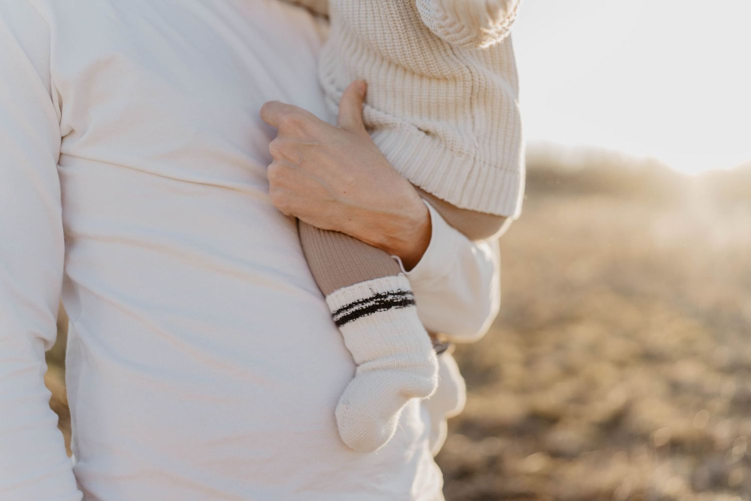 Close up of person wearing white sweater and bracelet against sunset backdrop.