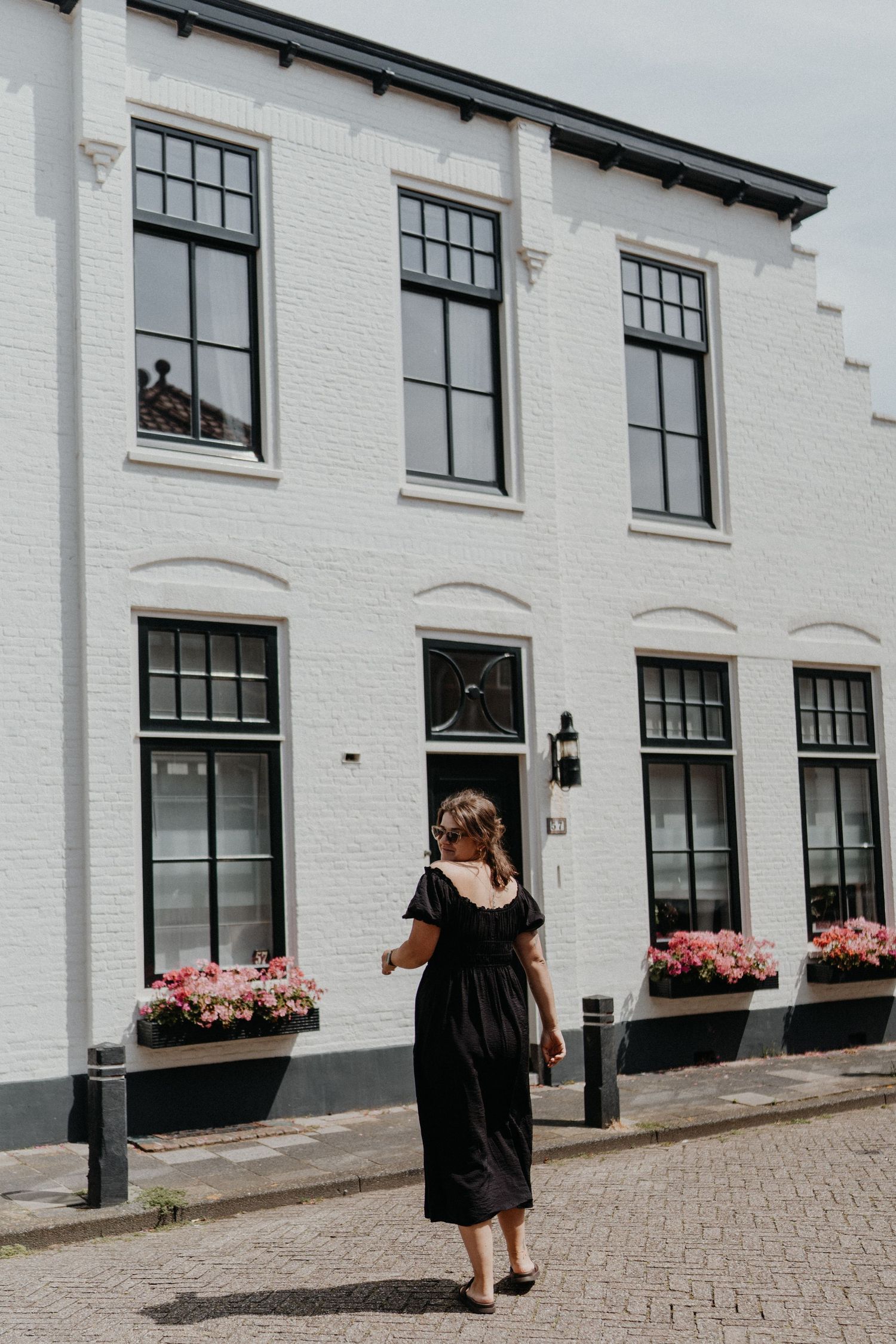 Woman in black dress standing before a classic white building with flower boxes.