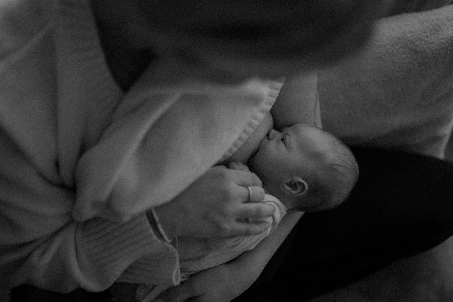 Black and white intimate portrait of parent feeding newborn baby.