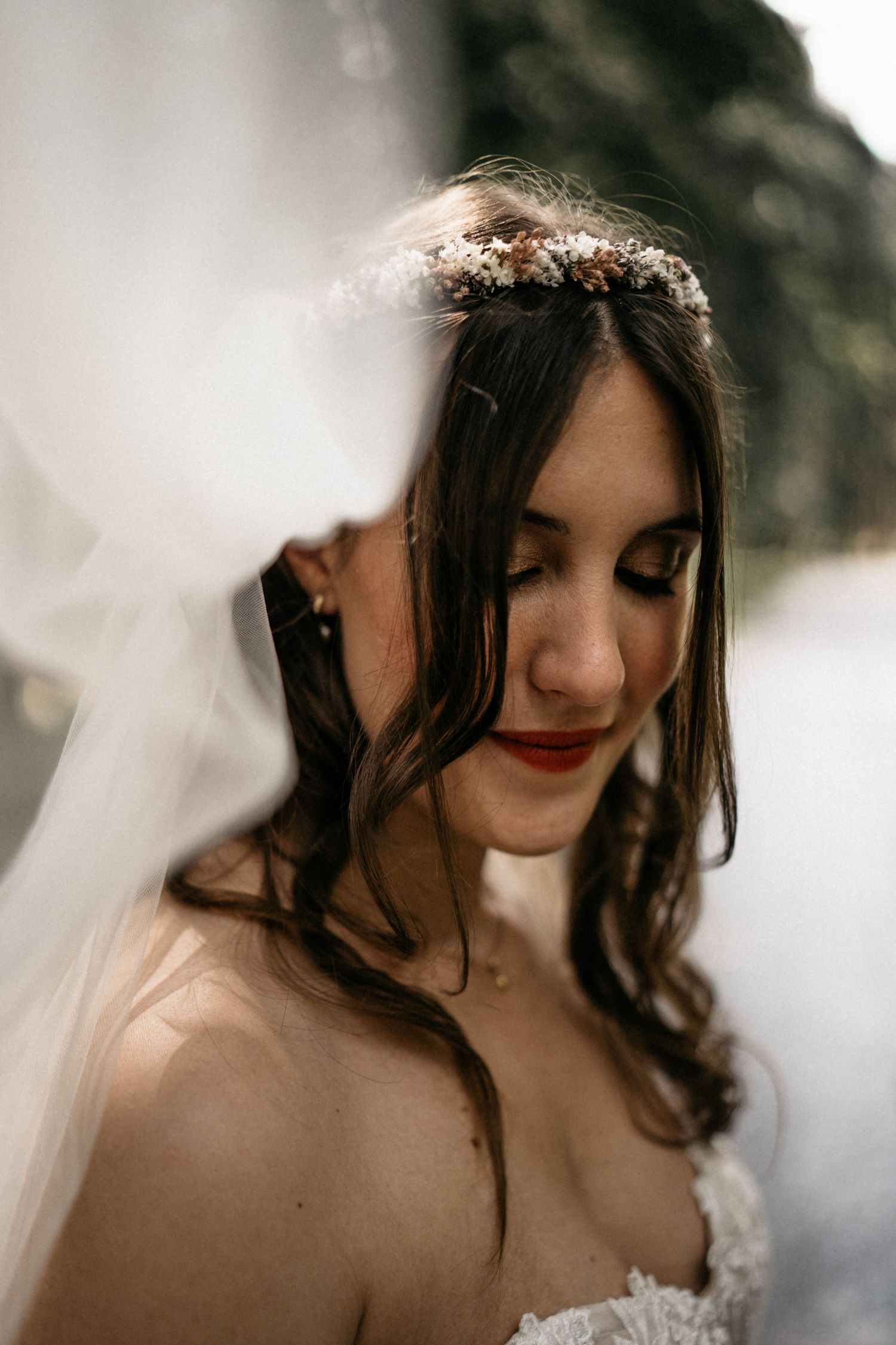 A bride wearing a floral crown and strapless wedding gown looks down with a soft smile.