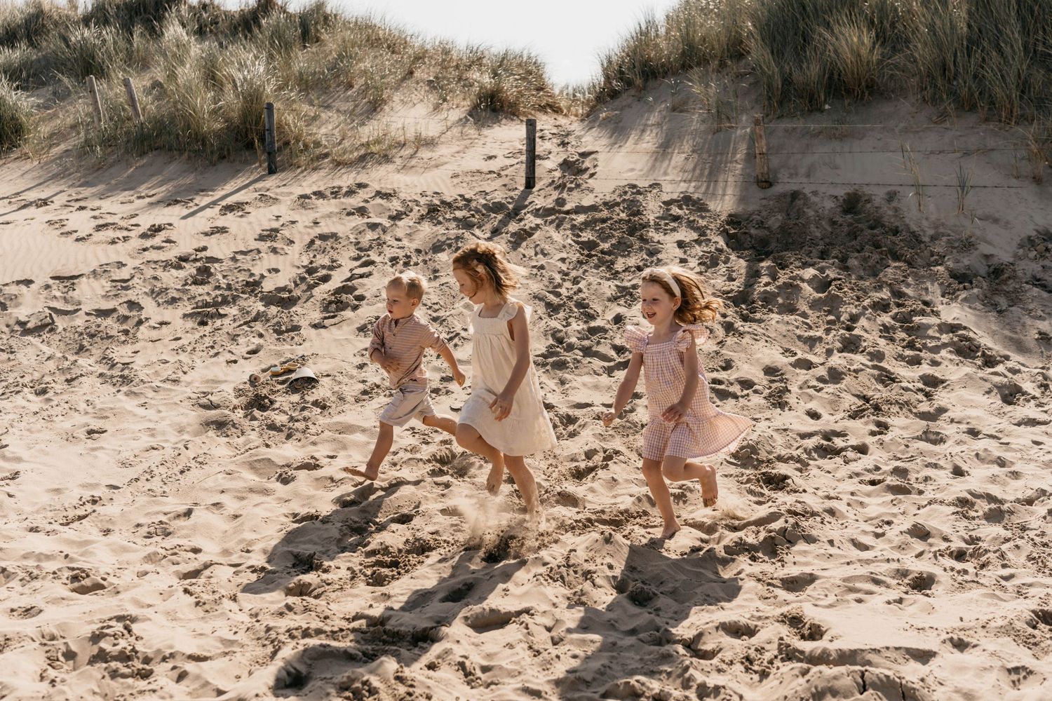 Children running and playing on sandy beach dunes during golden hour.