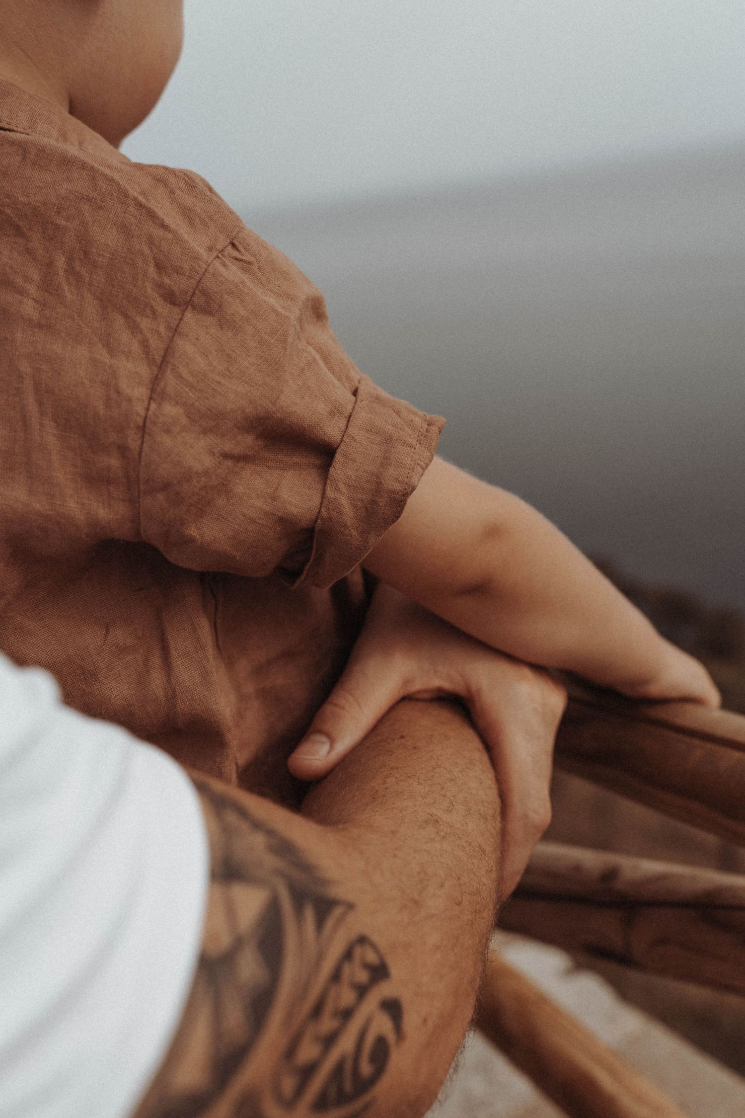 Close-up shot showing a person's arm wearing a brown linen shirt, with a detailed tribal tattoo visible on their forearm.