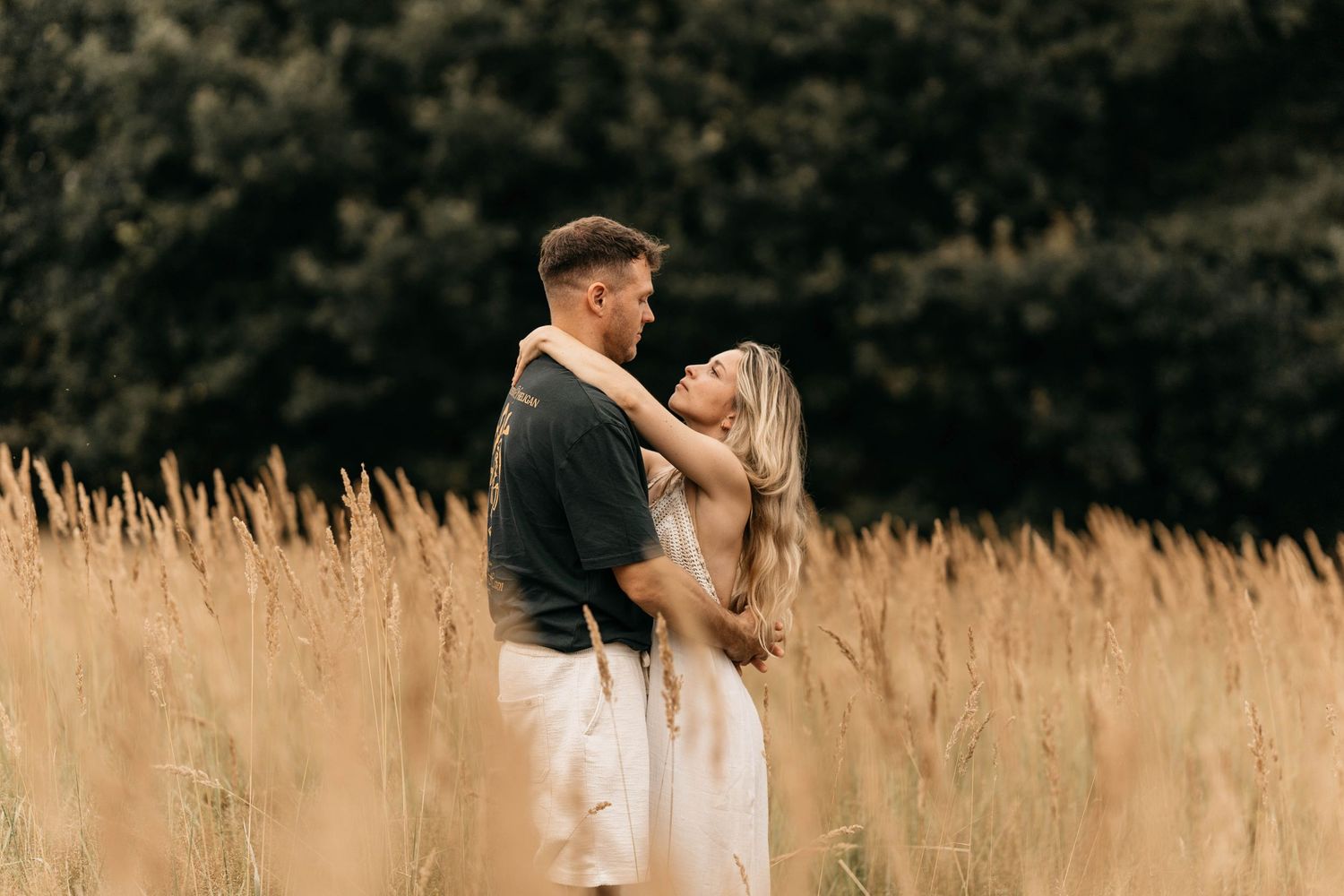 Couple sharing intimate moment while standing in golden wheat field at sunset.