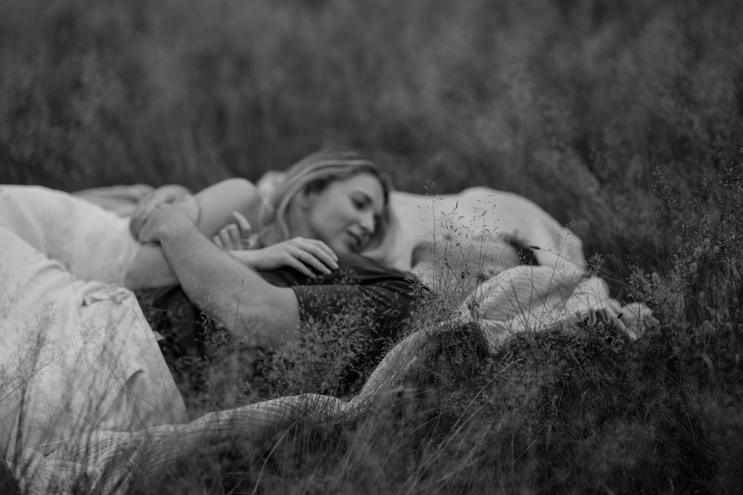Dreamy black and white photo of person lying in tall grass wearing flowing dress.