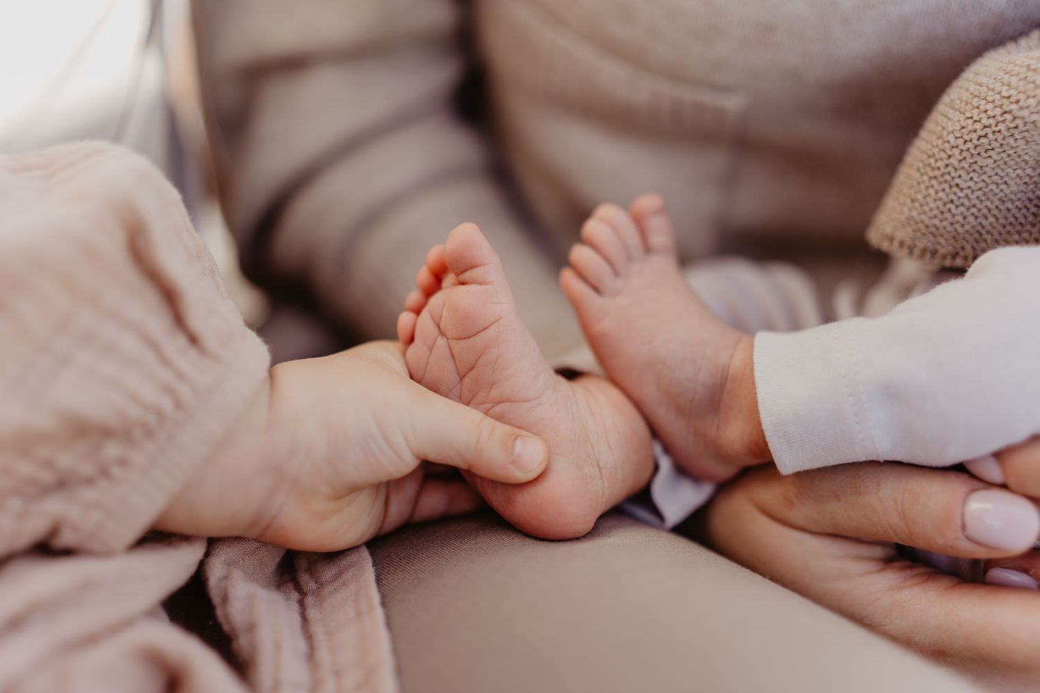 Close-up view of tiny baby feet being gently held by adult hands in soft neutral tones.