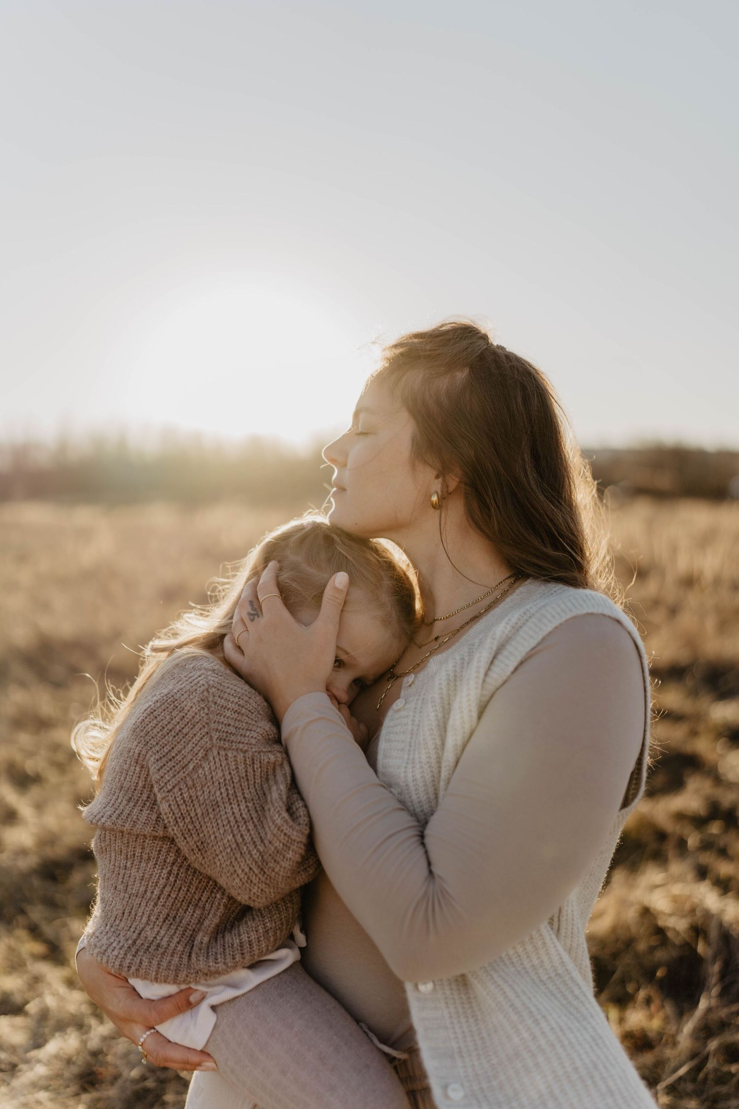 Tender moment between parent and child in warm sunlight against neutral background.