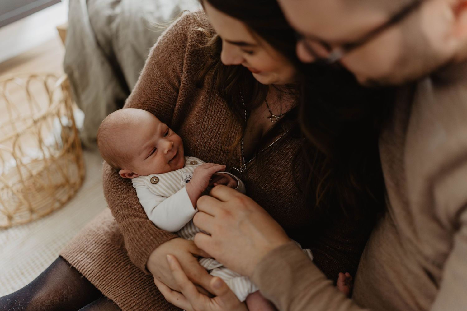 A tender moment between parent and newborn baby in a cozy brown sweater.