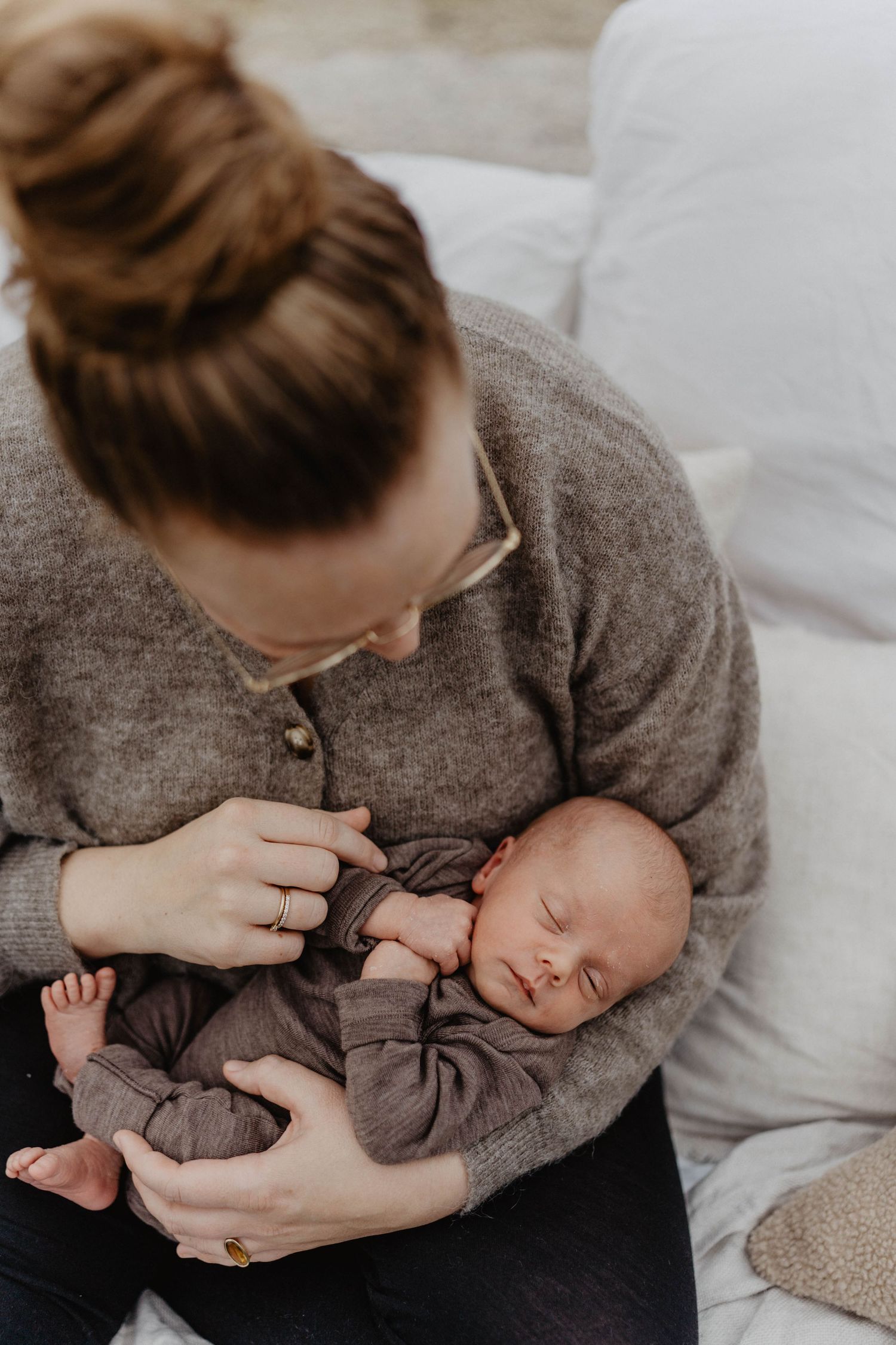 Baby in gray outfit being cradled while sleeping on soft couch.