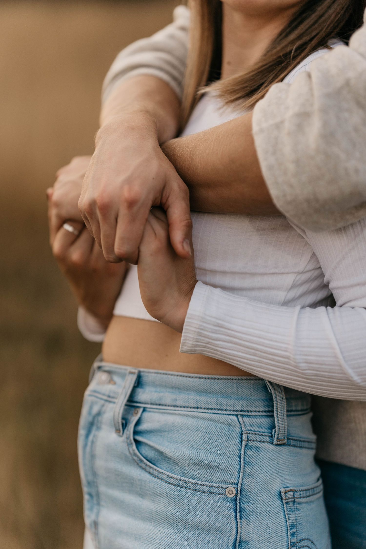 Close-up shot of couple's hands embracing around waist in casual denim and white clothing.