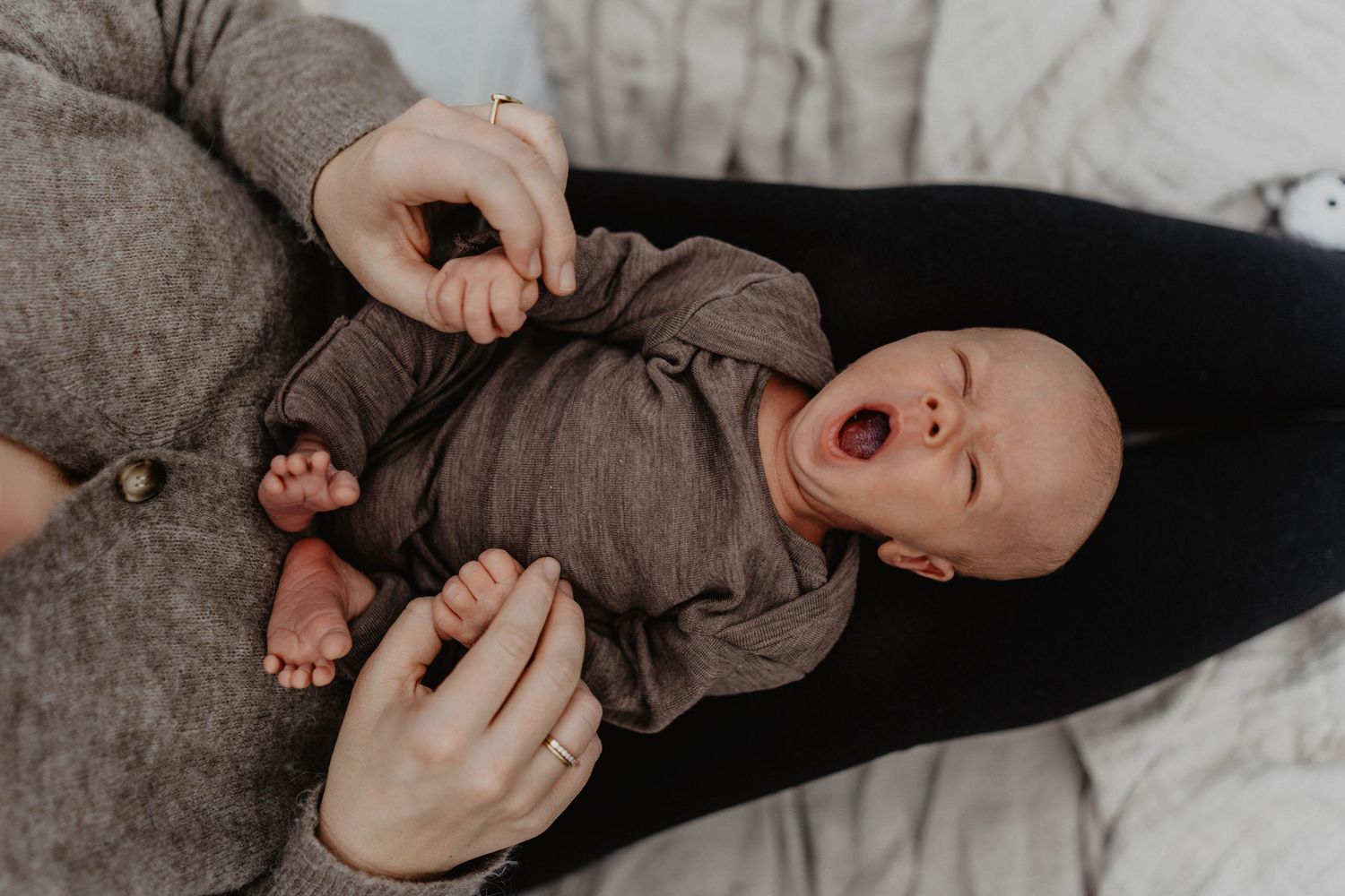 Baby in gray clothing yawning while being held.