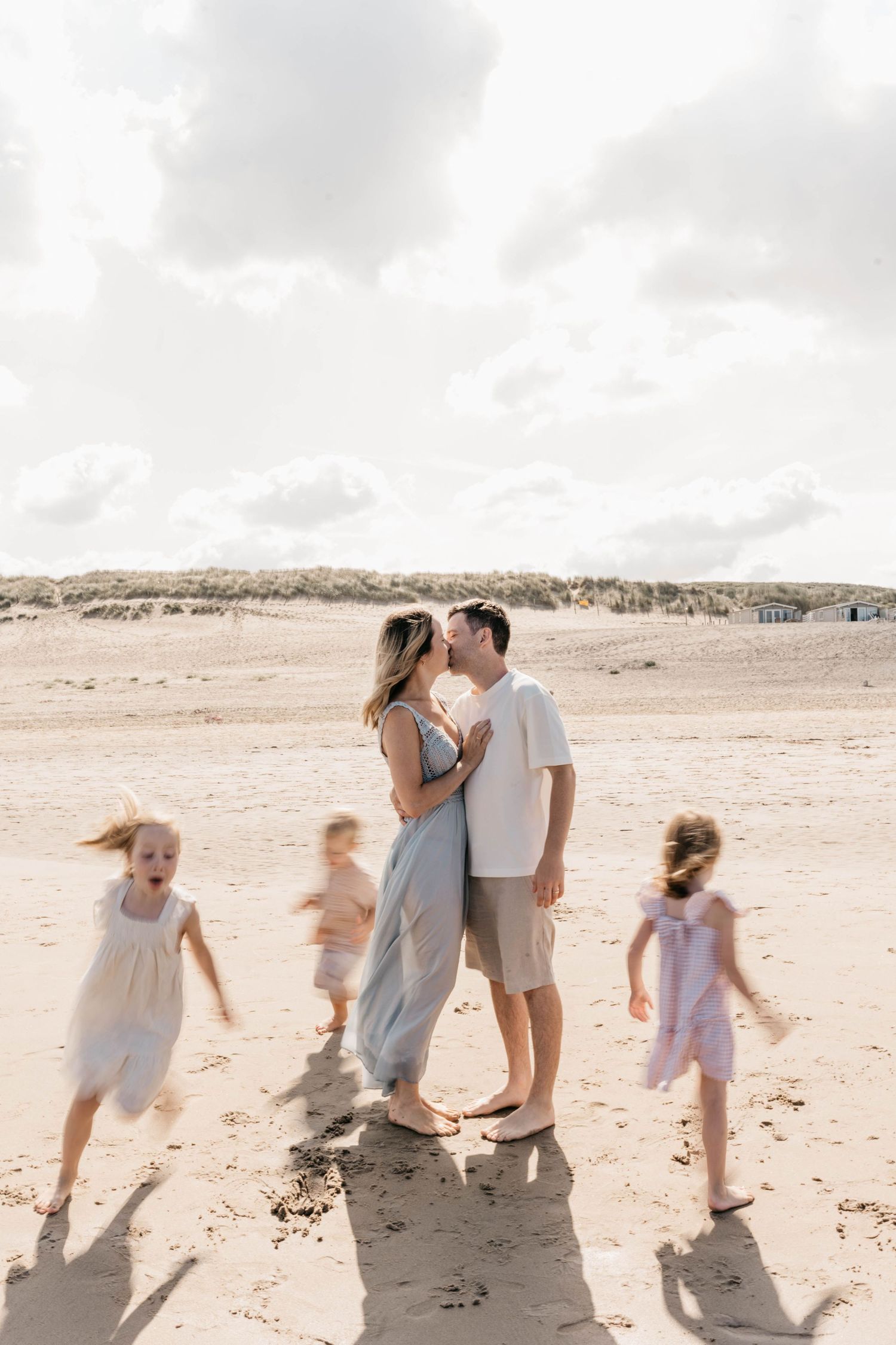 Family moment at the beach with children running in the background during sunset.