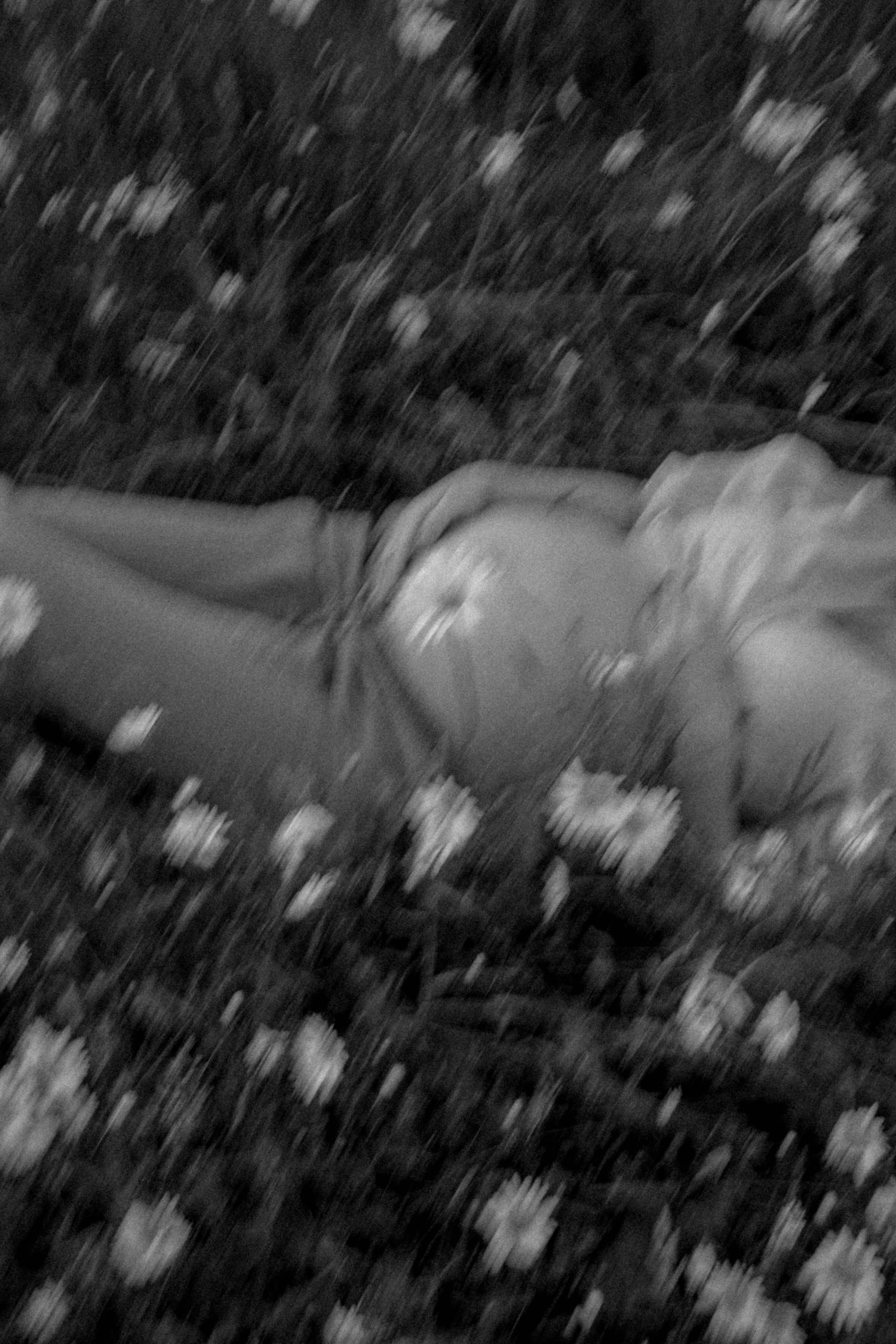 A black and white artistic photo of someone lying among flowers.