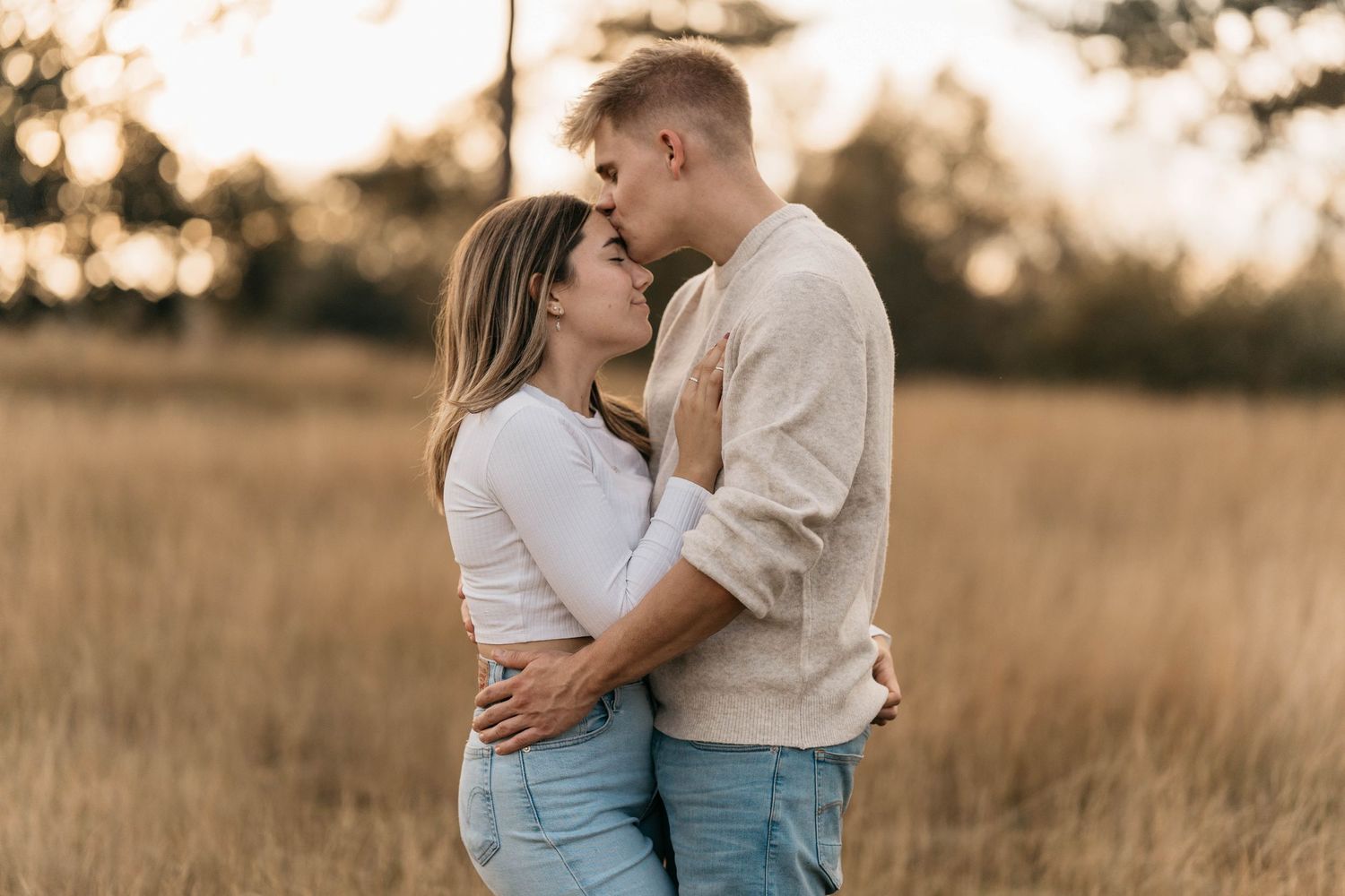 Intimate moment between couple in casual attire embracing in sunset field.