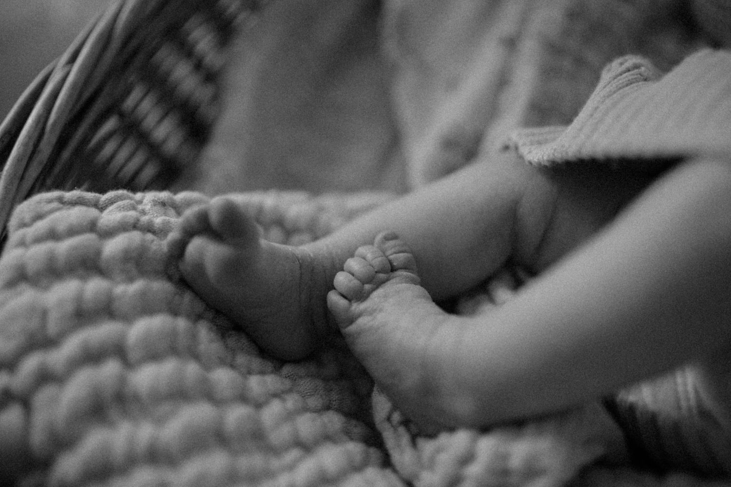 Close-up black and white photograph of tiny baby feet on textured blanket.