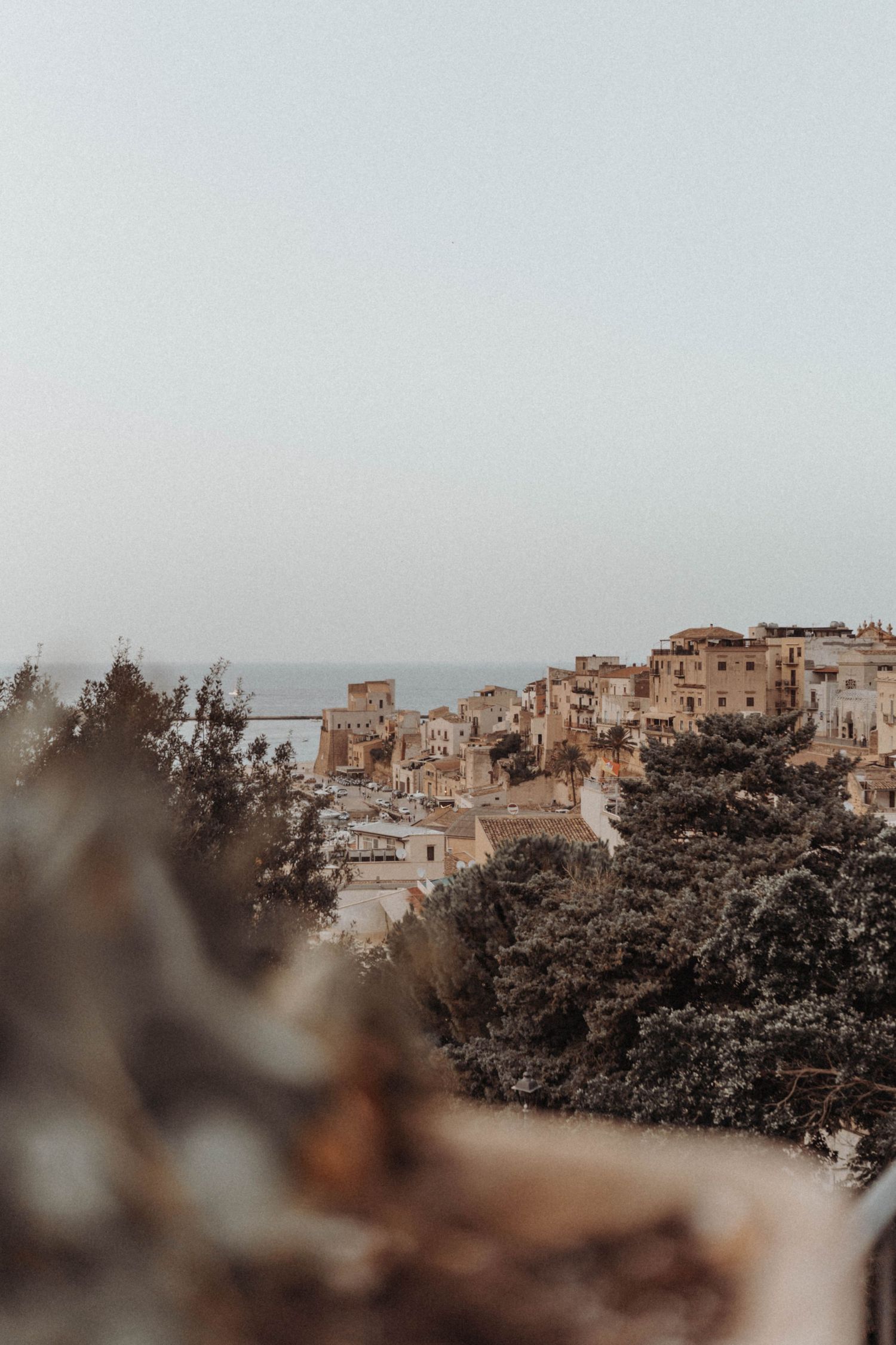 Aerial view of rustic Italian hillside village with beige stone buildings surrounded by trees and misty sky.