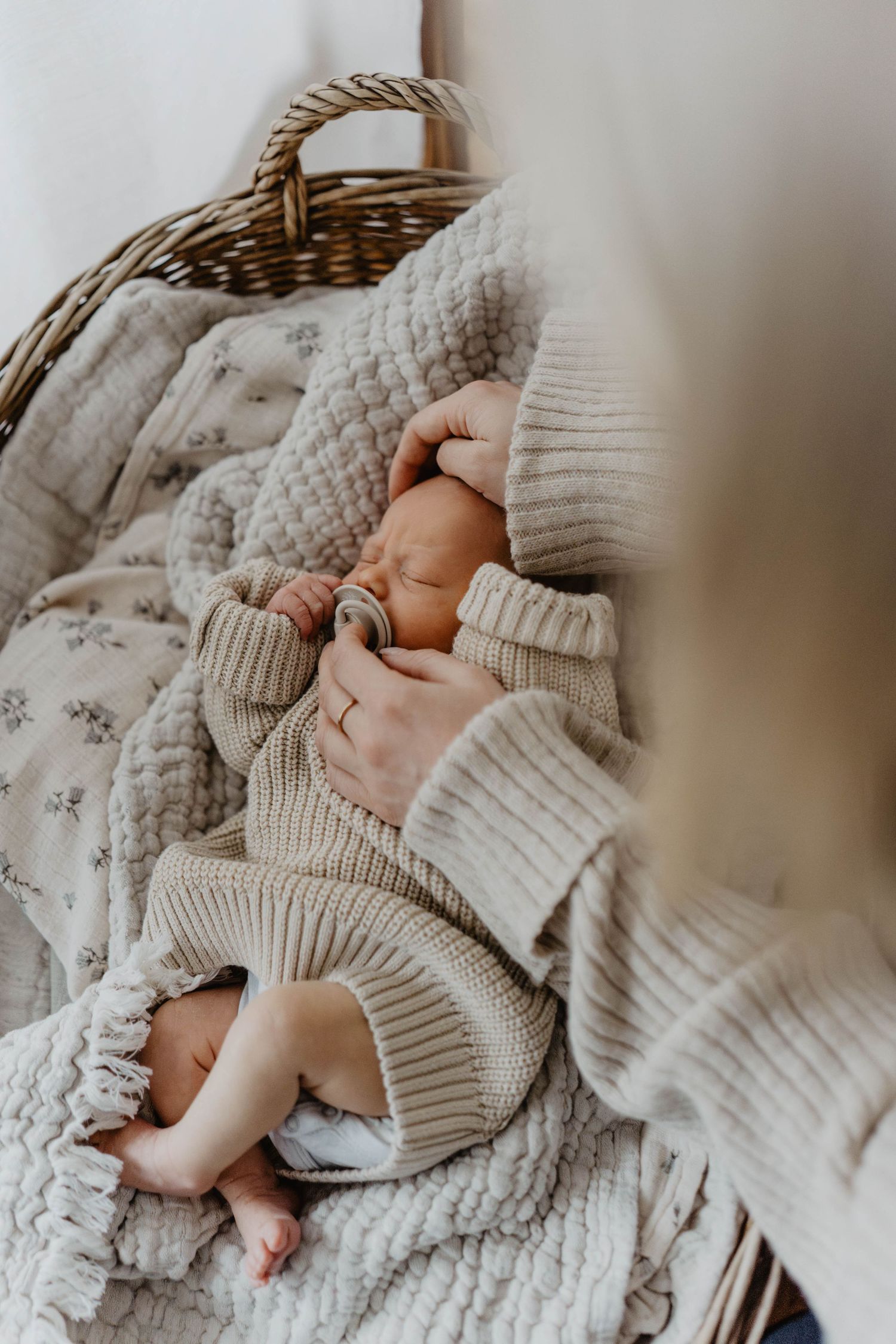 Gentle hands holding newborn baby dressed in cozy knit sweater in basket.