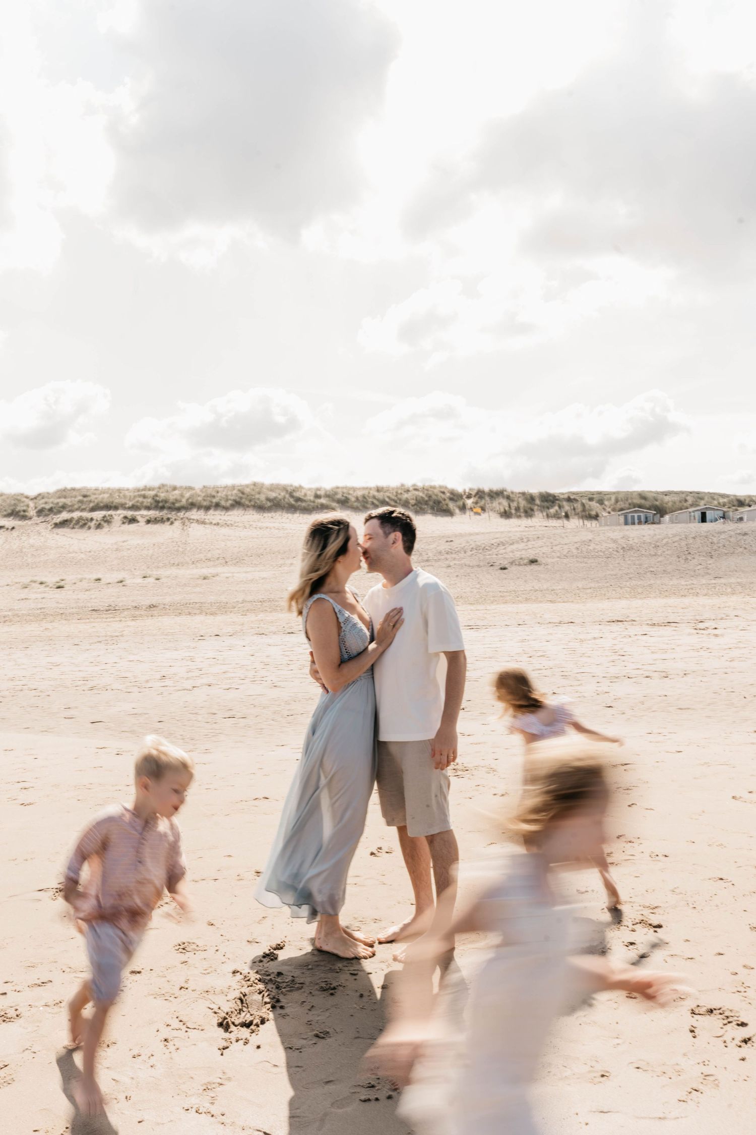 Family moment on beach with children running past during golden hour.