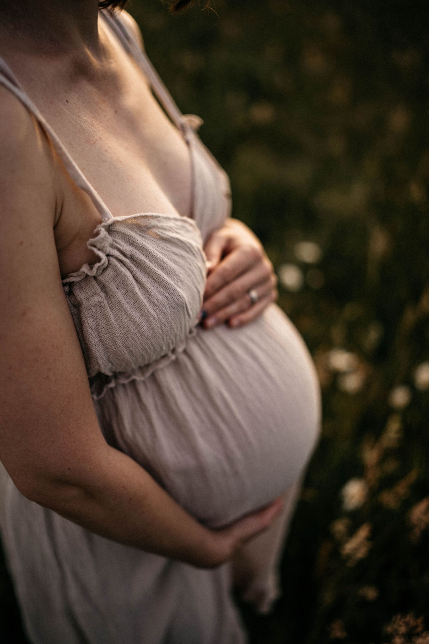 Close-up of pregnant belly in soft beige dress against dark background.
