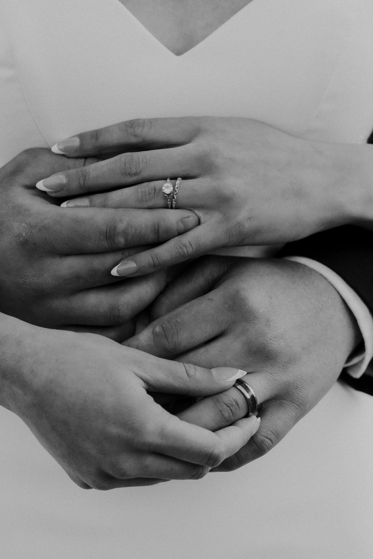 Black and white close-up of bride and groom hands displaying diamond engagement ring and wedding band.