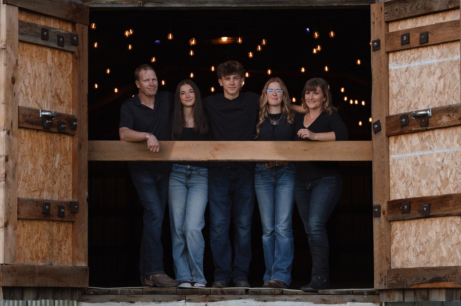 Five people posing together in a rustic barn doorway with warm bokeh lights in the background.