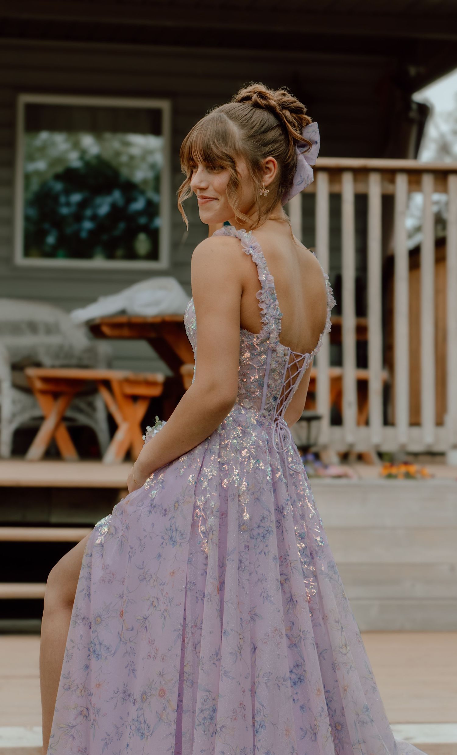 Young woman in lavender floral A-line prom gown with lace-up back and 3D floral details, posing outdoors.