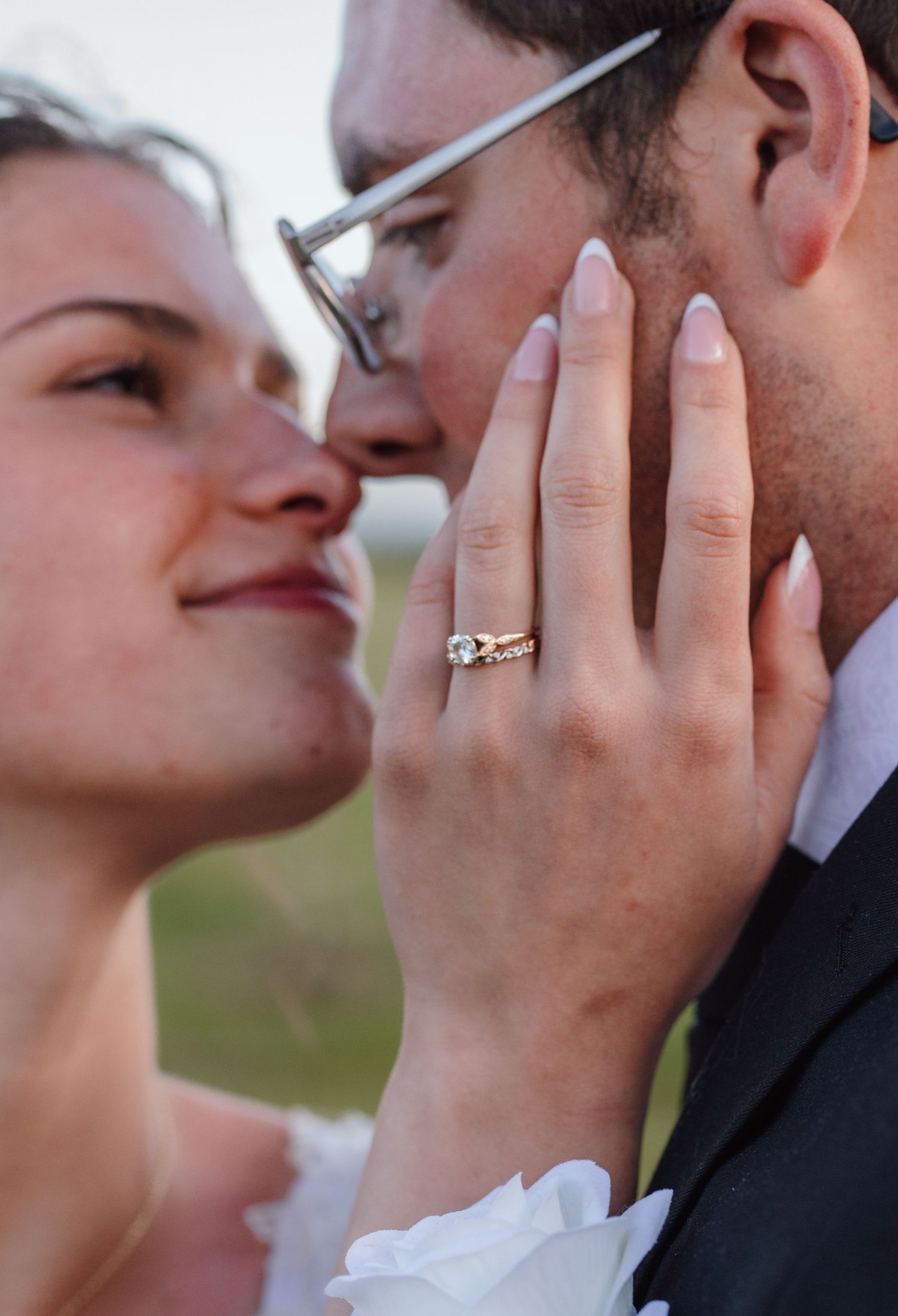Bride and groom share a romantic close-up moment, showcasing a stunning diamond engagement ring and wedding band on her hand.