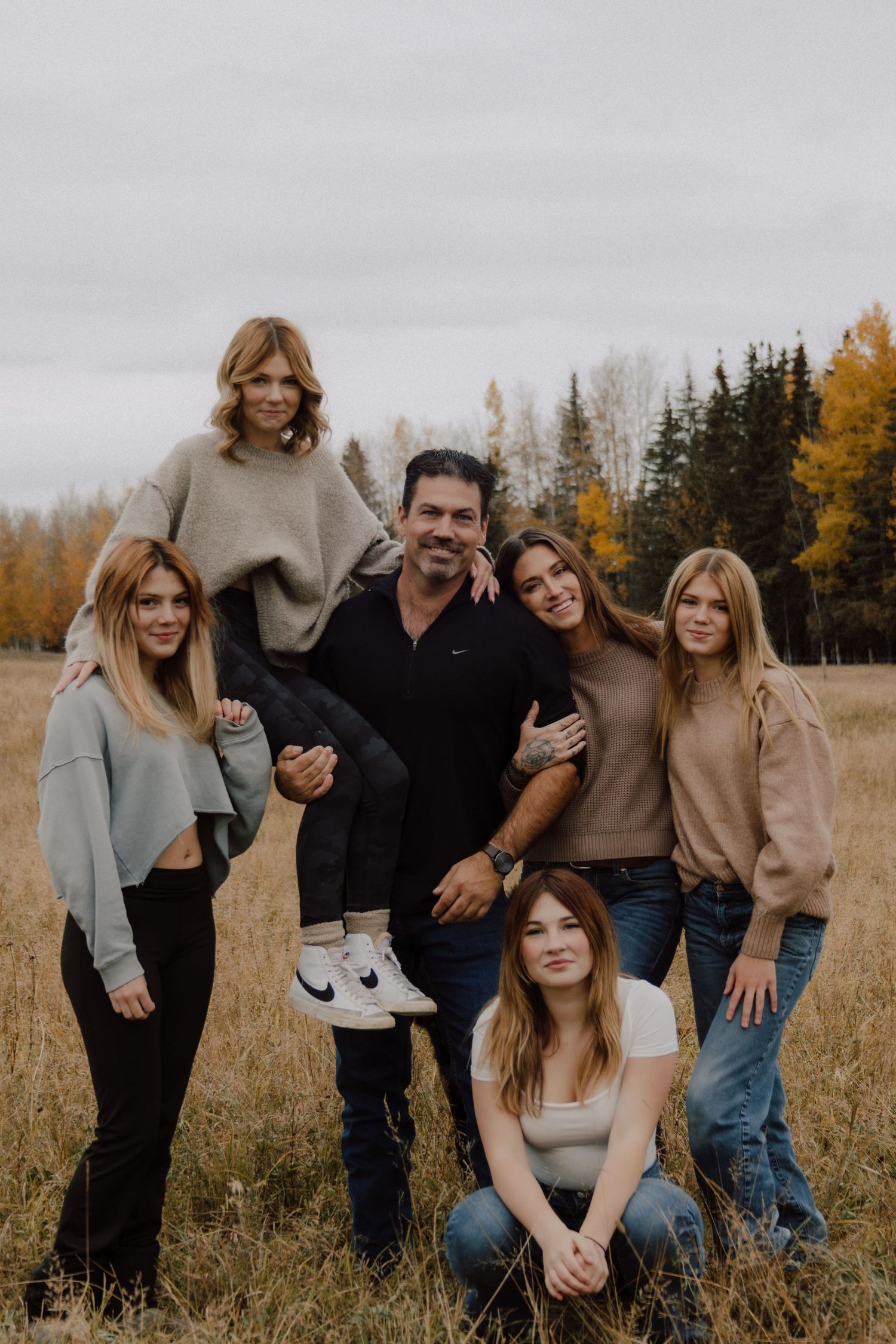 Family of six posing in autumn field with colorful fall foliage, man holding daughter on shoulders.