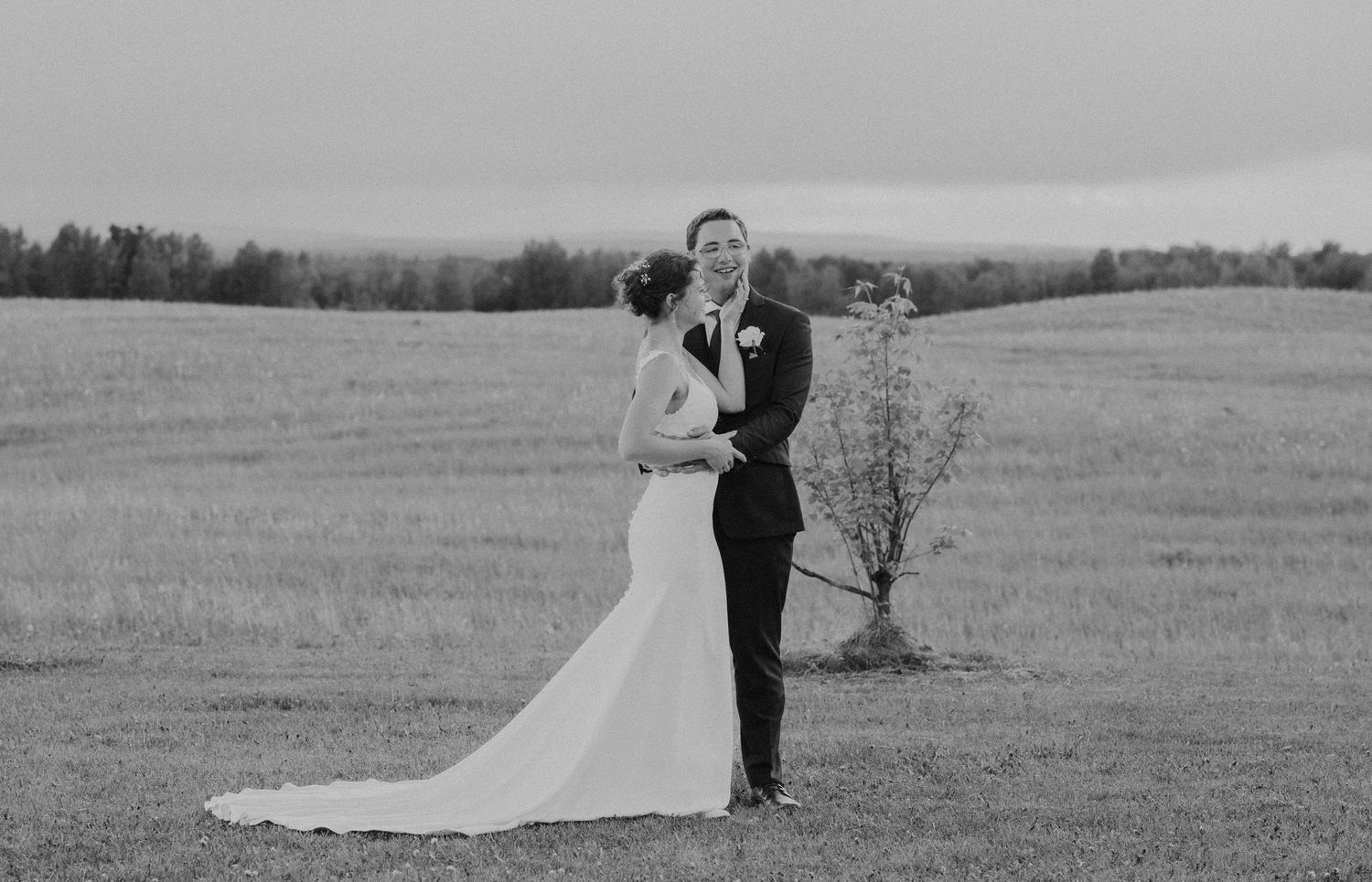 Black and white photo of a bride and groom embracing in an open field on their wedding day.