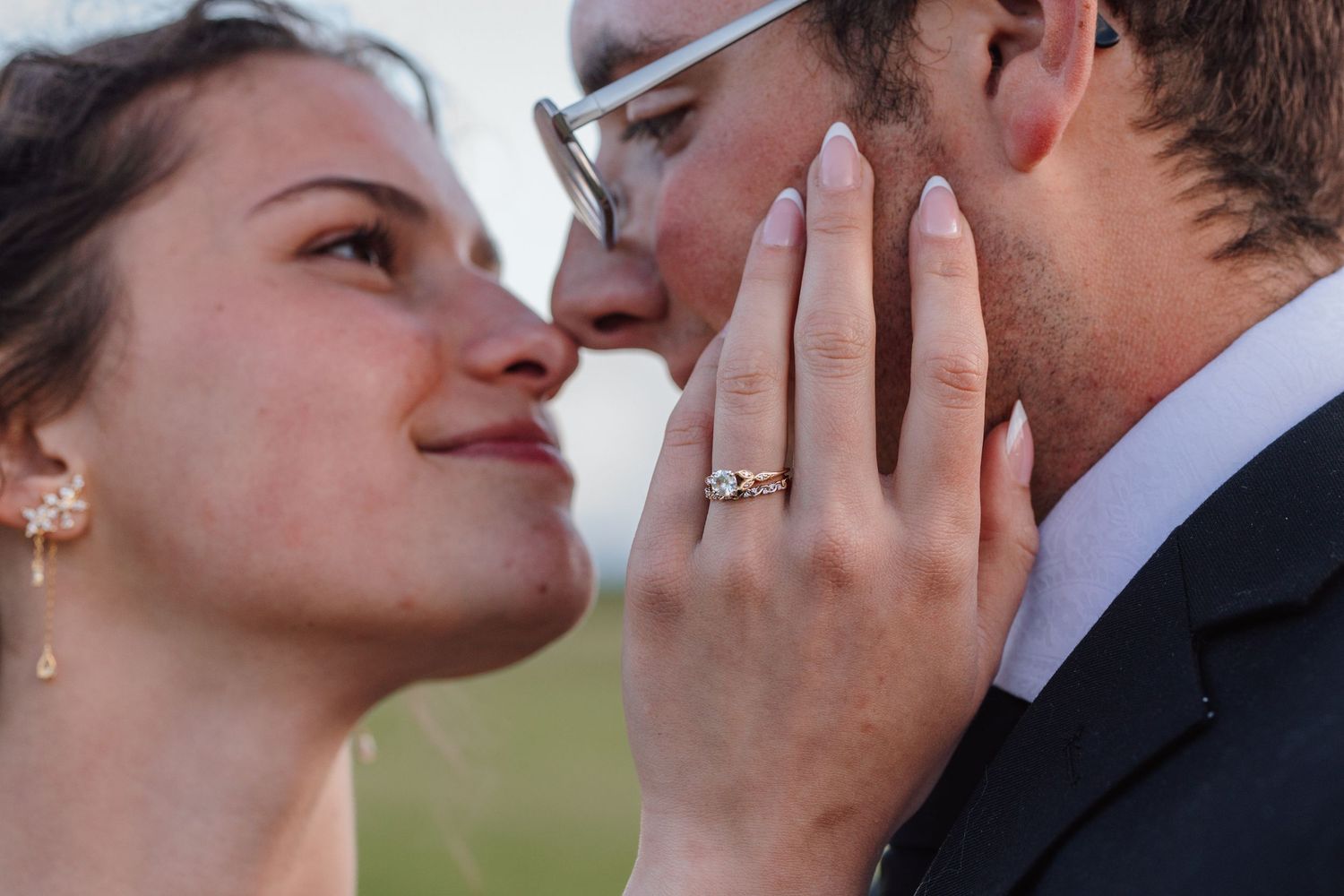 Close-up of bride and groom sharing a romantic moment, bride wearing diamond ring and pearl earring.