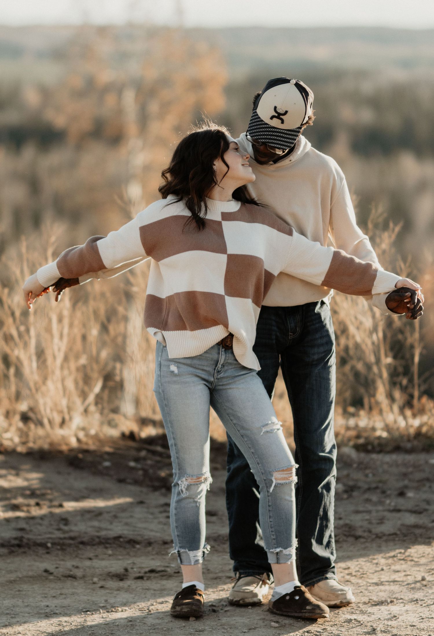 Couple kissing outdoors in a field, woman wearing brown checkered oversized sweater.