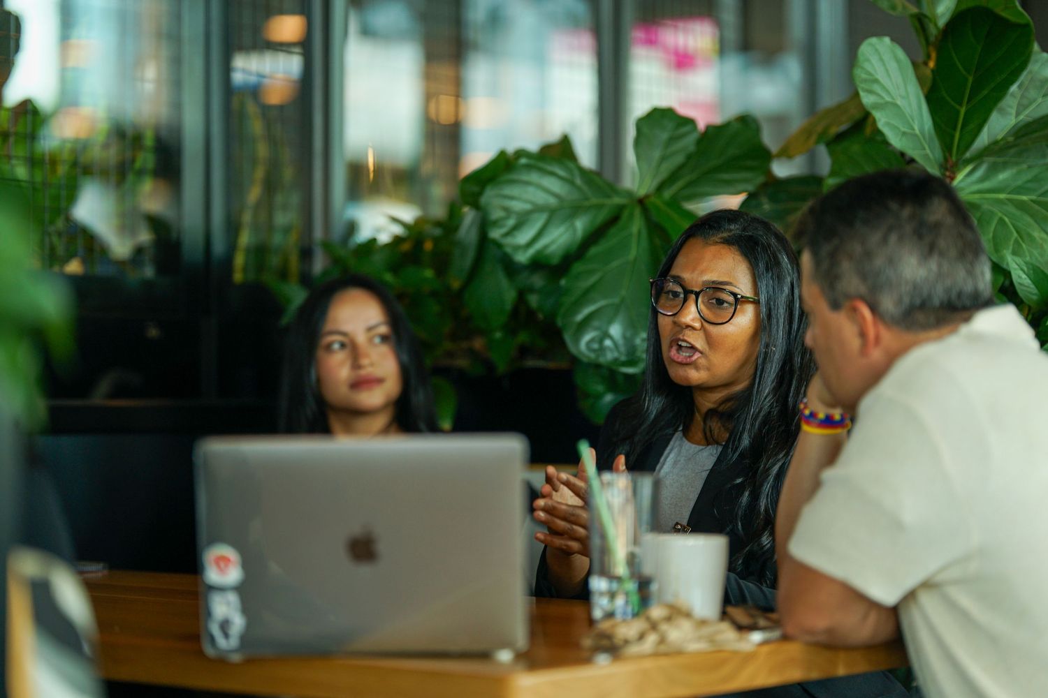 Two women and a man having a business meeting at a cafe table with an Apple laptop.