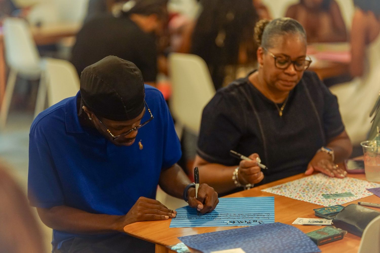 Two people focused on writing and drawing on colorful papers at a table during a group activity event.