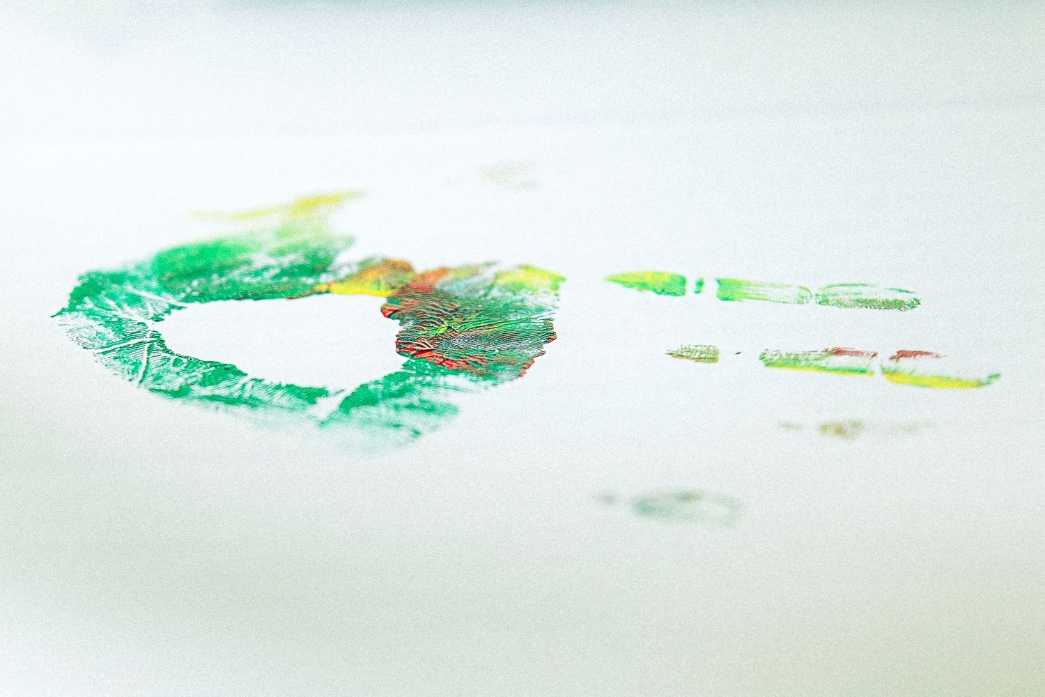 Green and red handprint art stamped on white paper, creating a colorful circular fingerprint design.