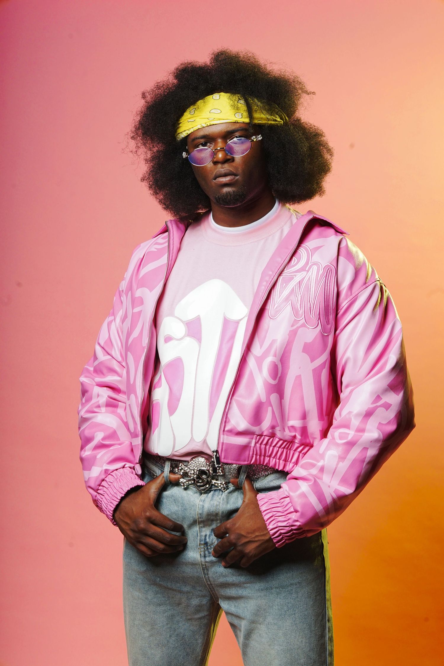 Model in pink bomber jacket and graphic tee against gradient background.