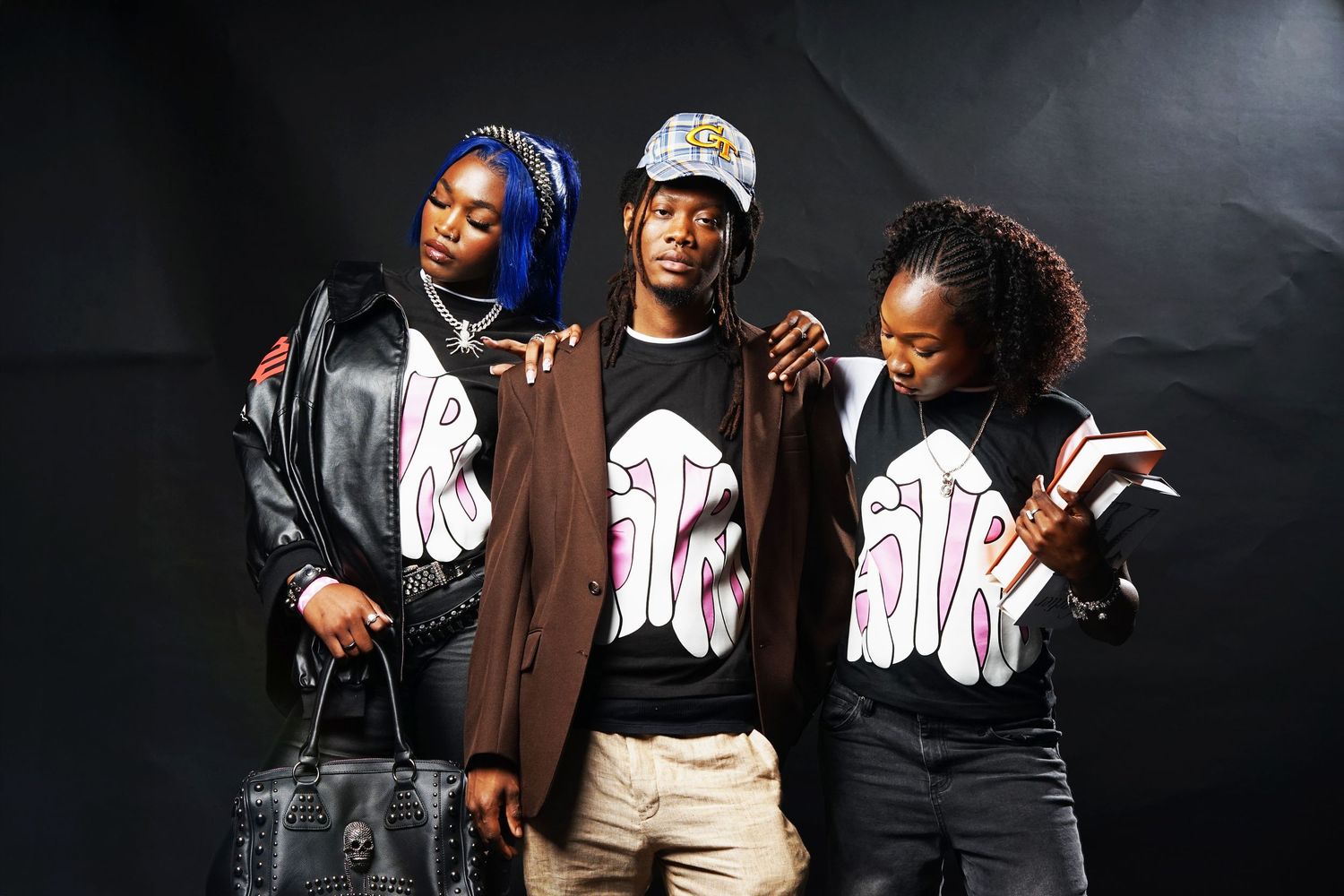Three models in coordinated streetwear outfits posing casually against dark background.