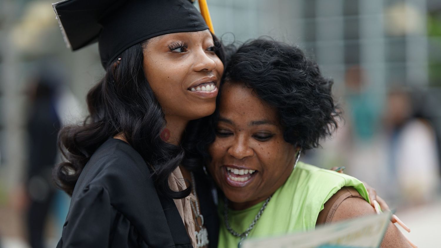 Joyful embrace between graduate and loved one during outdoor graduation celebration.