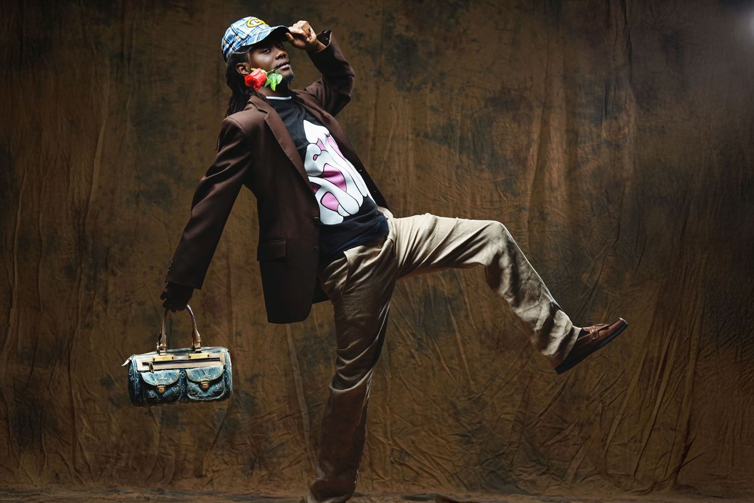 A dynamic fashion shot of someone in business attire and blue cap striking a dramatic pose against a dark background.