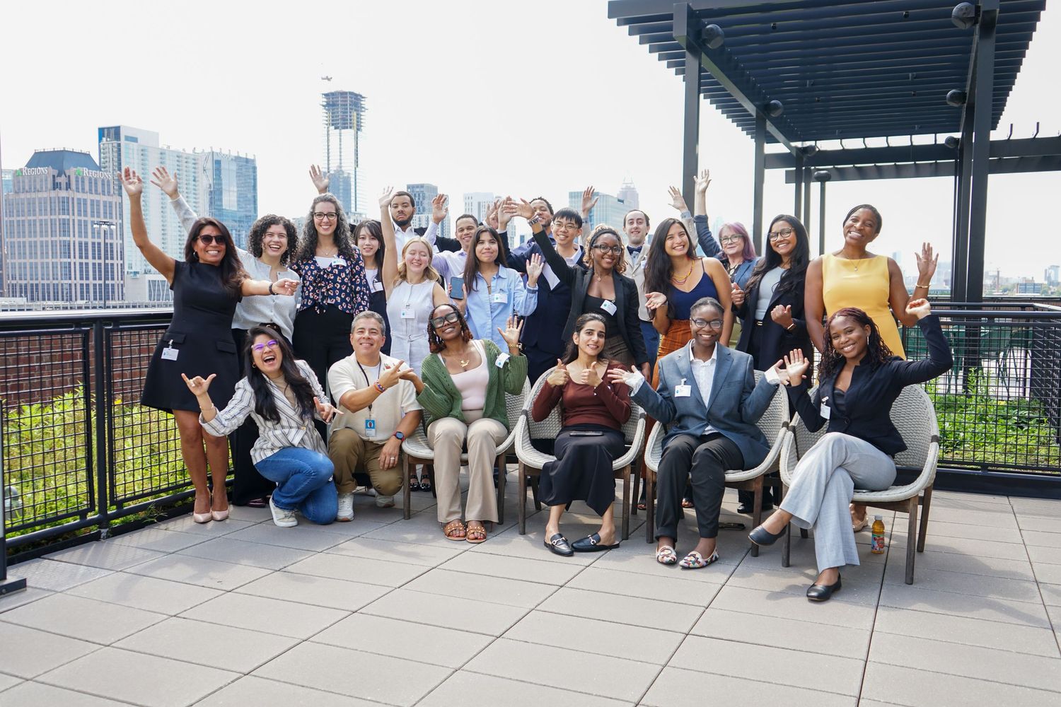 Large diverse group of professionals posing together on a rooftop terrace with city skyline views.