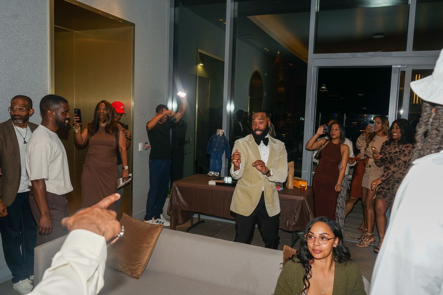 Elegant party gathering with guests in formal attire socializing in a modern venue with large windows.
