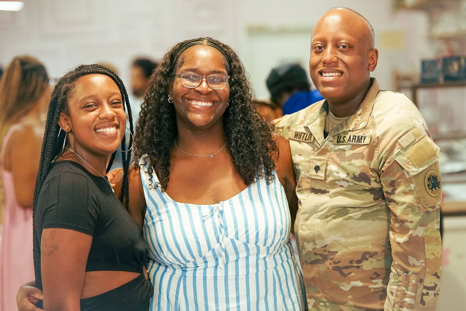 Two women and a US Army soldier smile together for a photo at an indoor event.